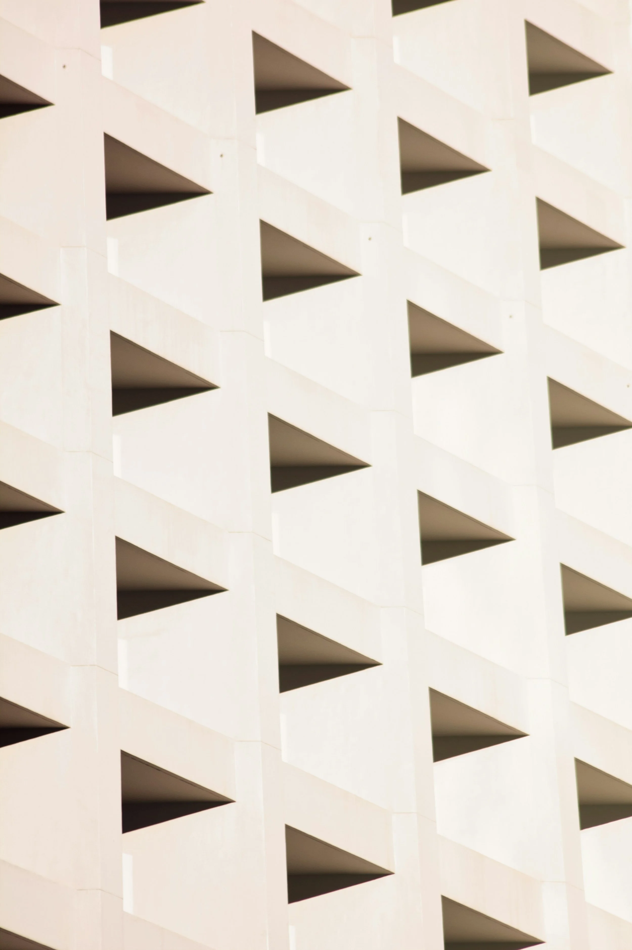 A close-up view of a modern building's exterior with a repeating pattern of balconies with diagonal walls and rectangular openings.