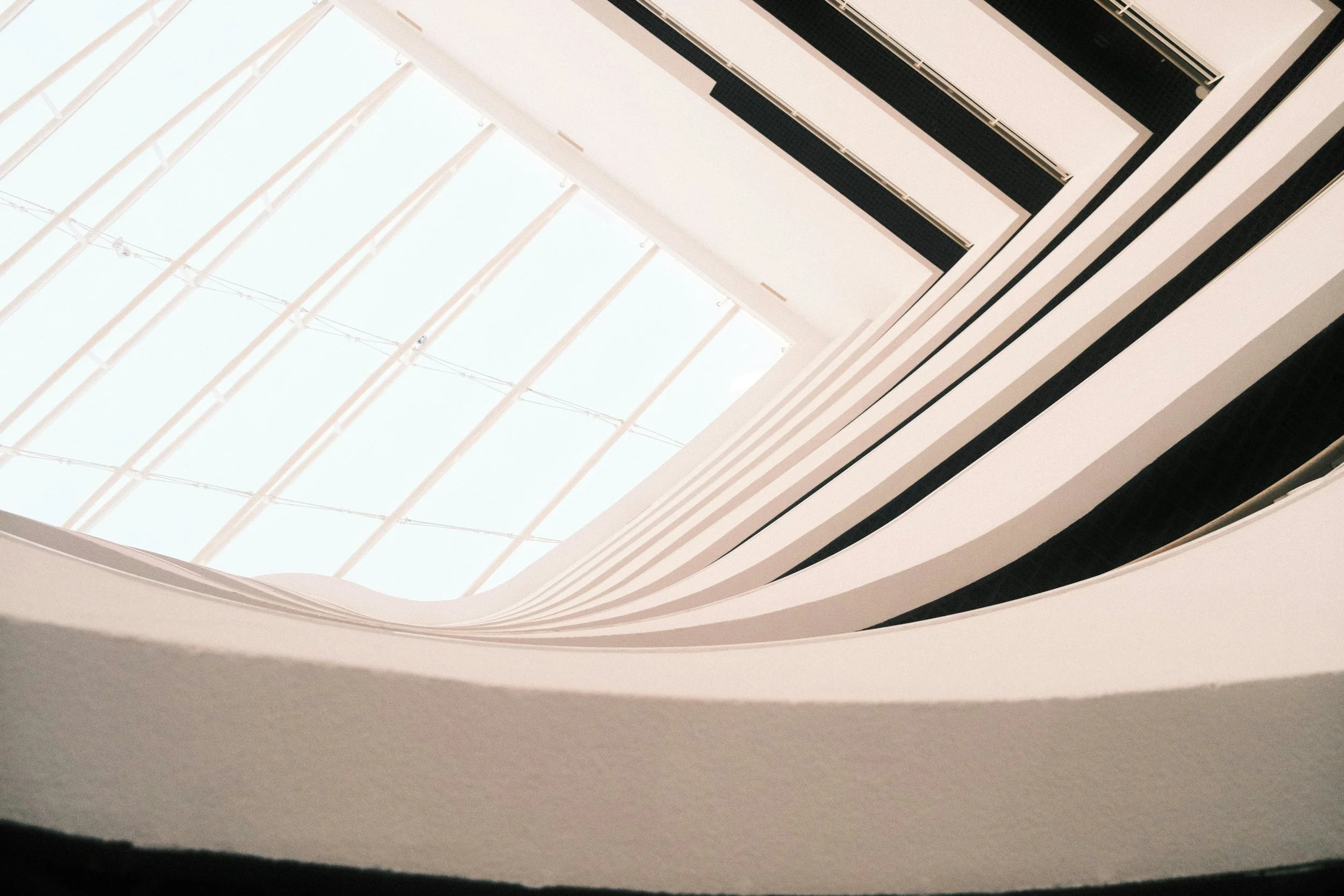 Looking up at a modern architectural interior with curved white walls and a large glass skylight ceiling
