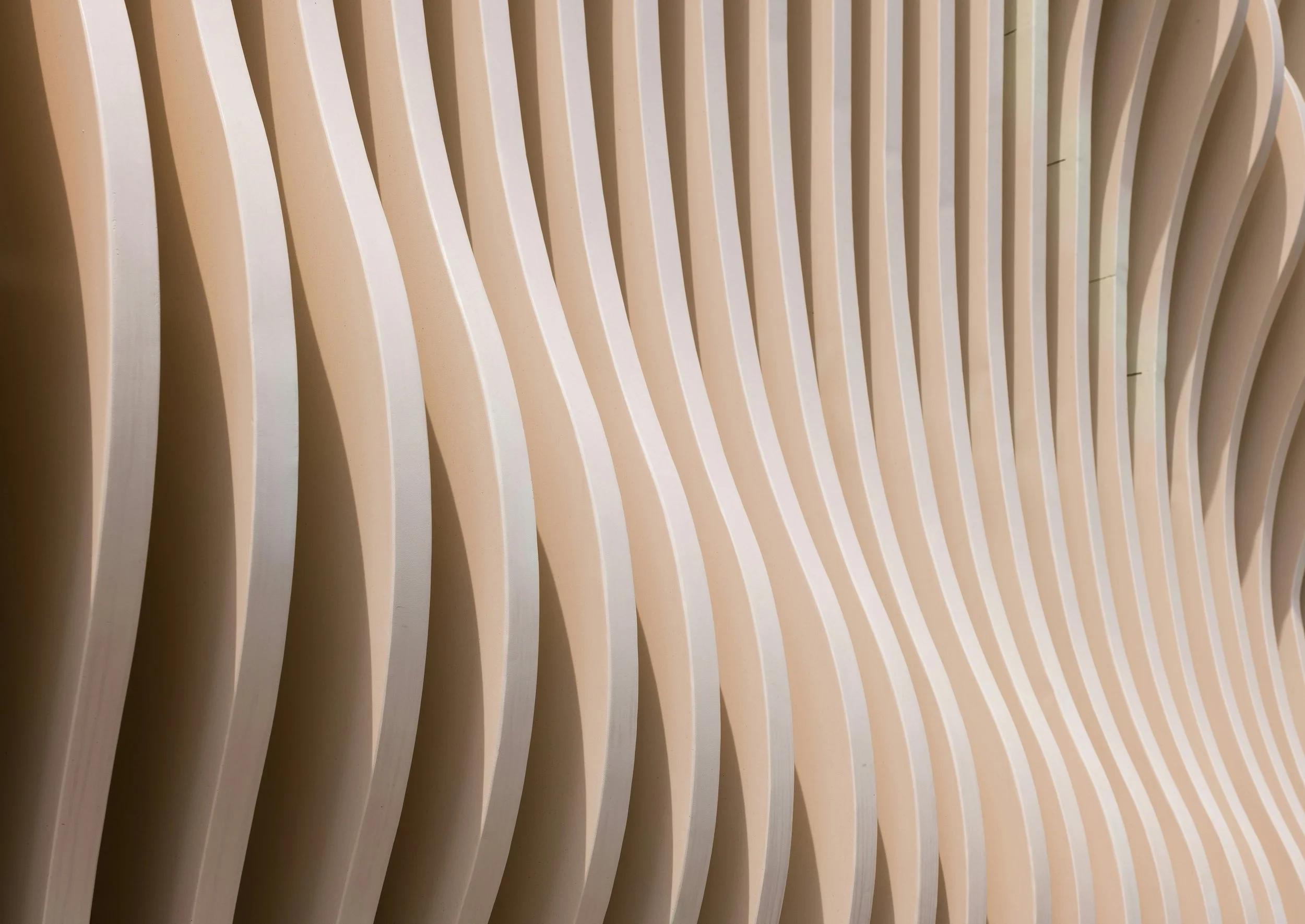 Close-up view of a beige, curved, slatted wooden wall with evenly spaced vertical slats.