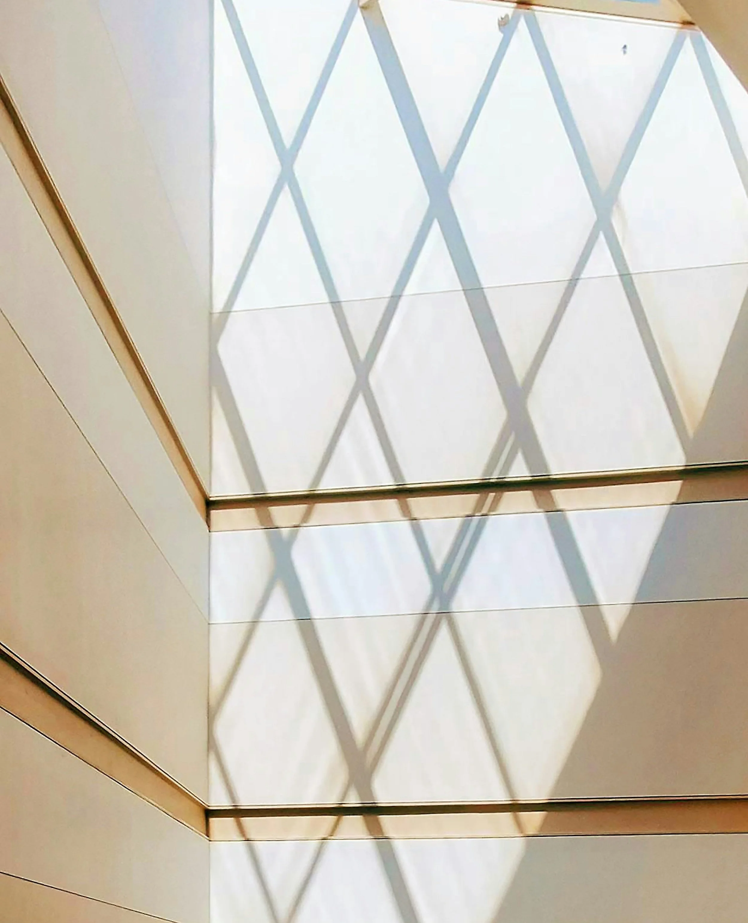 Shadow of a lattice pattern cast on a ceiling with beige panels and wooden trim.