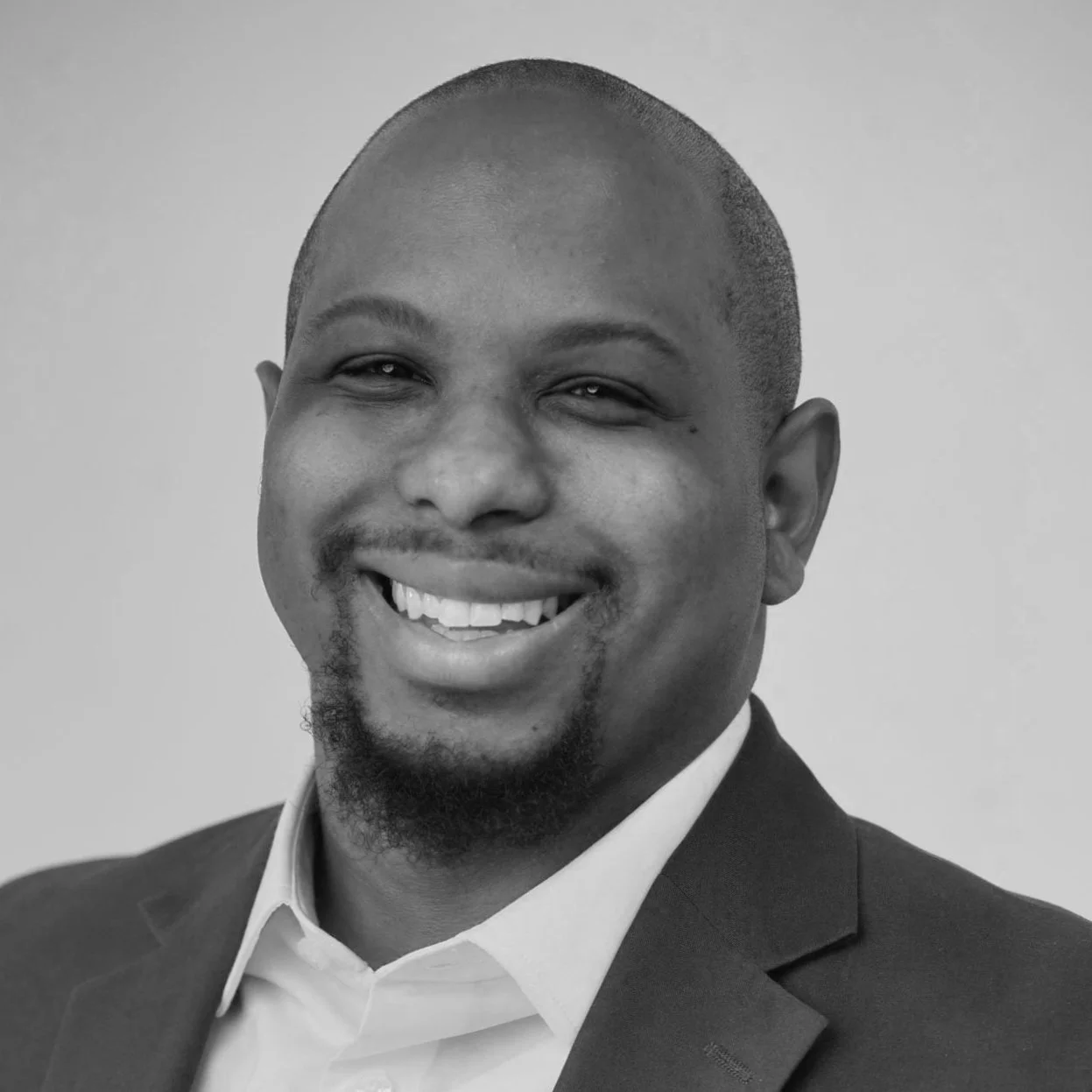Black and white portrait of a smiling man wearing a suit and white shirt, with a closely shaved head and goatee.