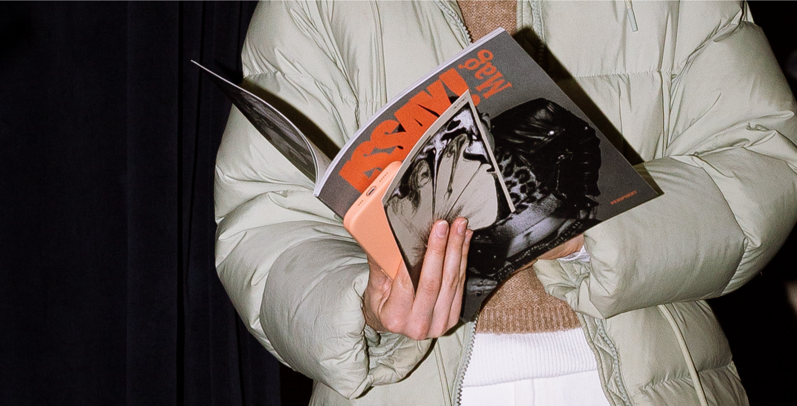 Person wearing a cream-colored jacket holding and reading ISSAY! magazine