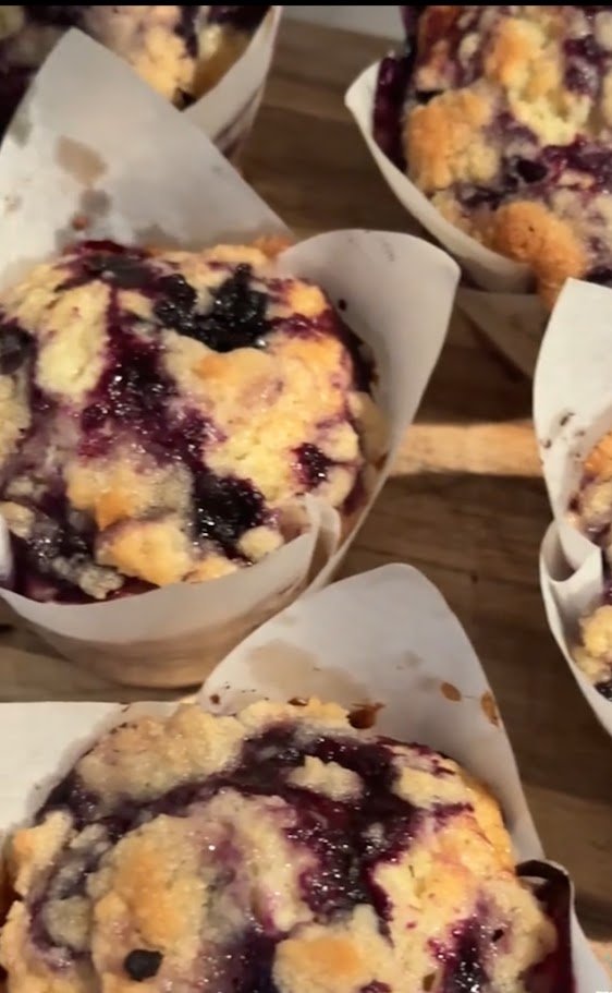 Apple blueberry cobbler muffins topped with crumbly streusel in white paper cups on a wooden surface.