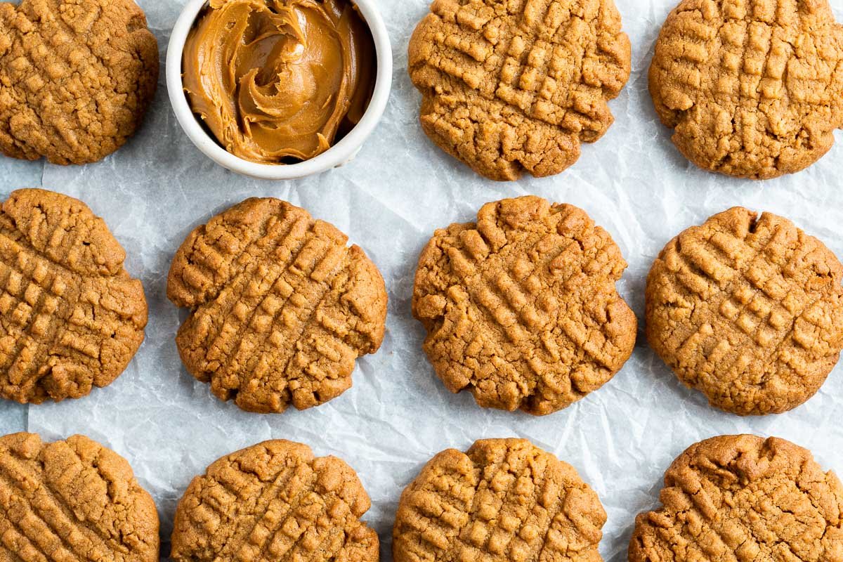 A tray of twelve peanut butter cookies with a jar of peanut butter in the center.