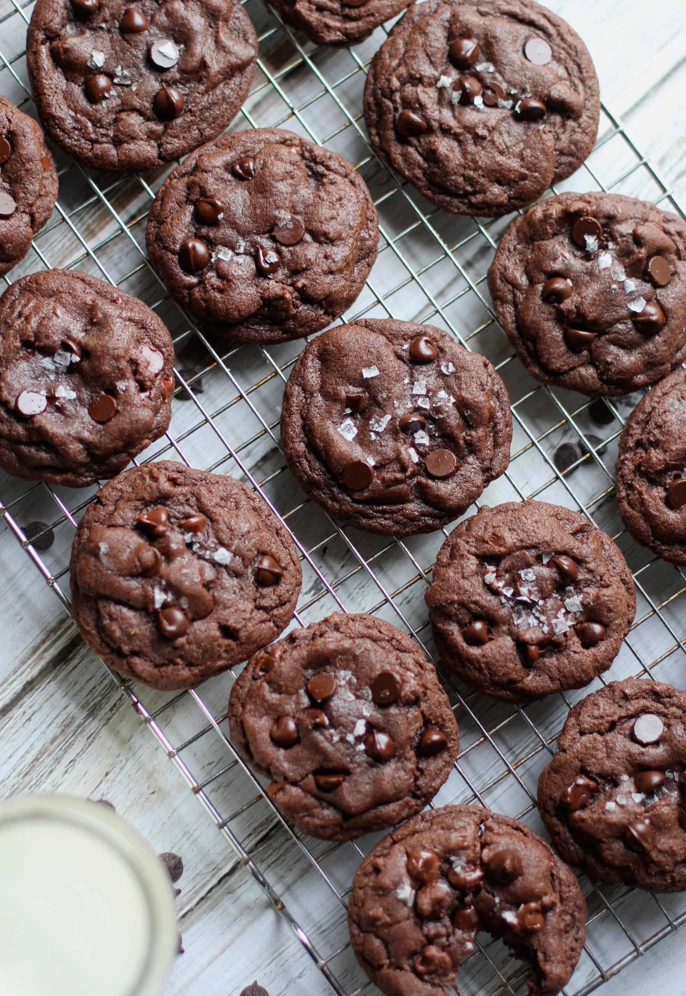 Chocolate chip cookies with sea salt on a wire cooling rack, with a glass of milk partially visible in the corner.
