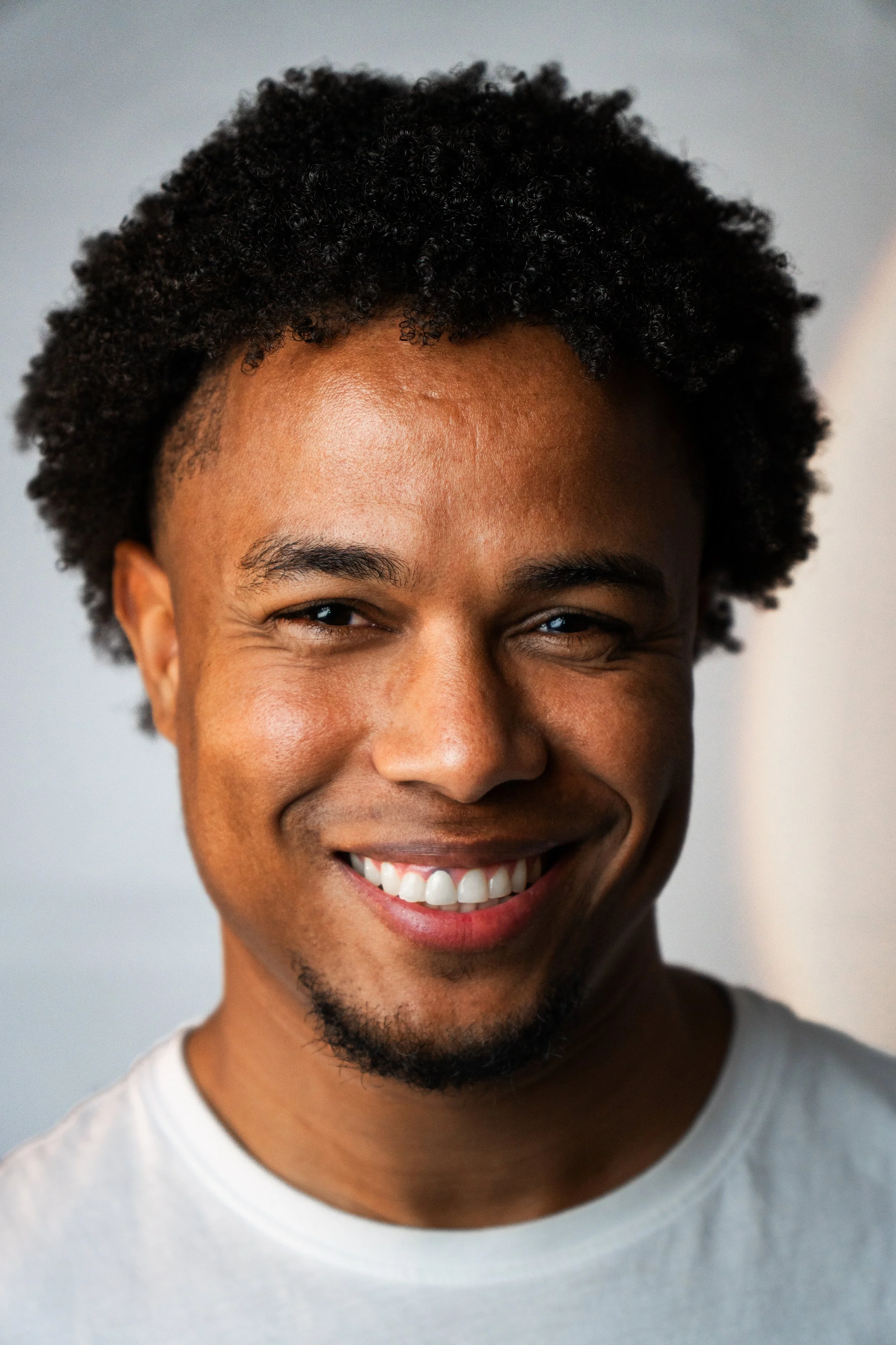 Ragazzo sorridente con capelli afro, pelle scura, e maglietta bianca.