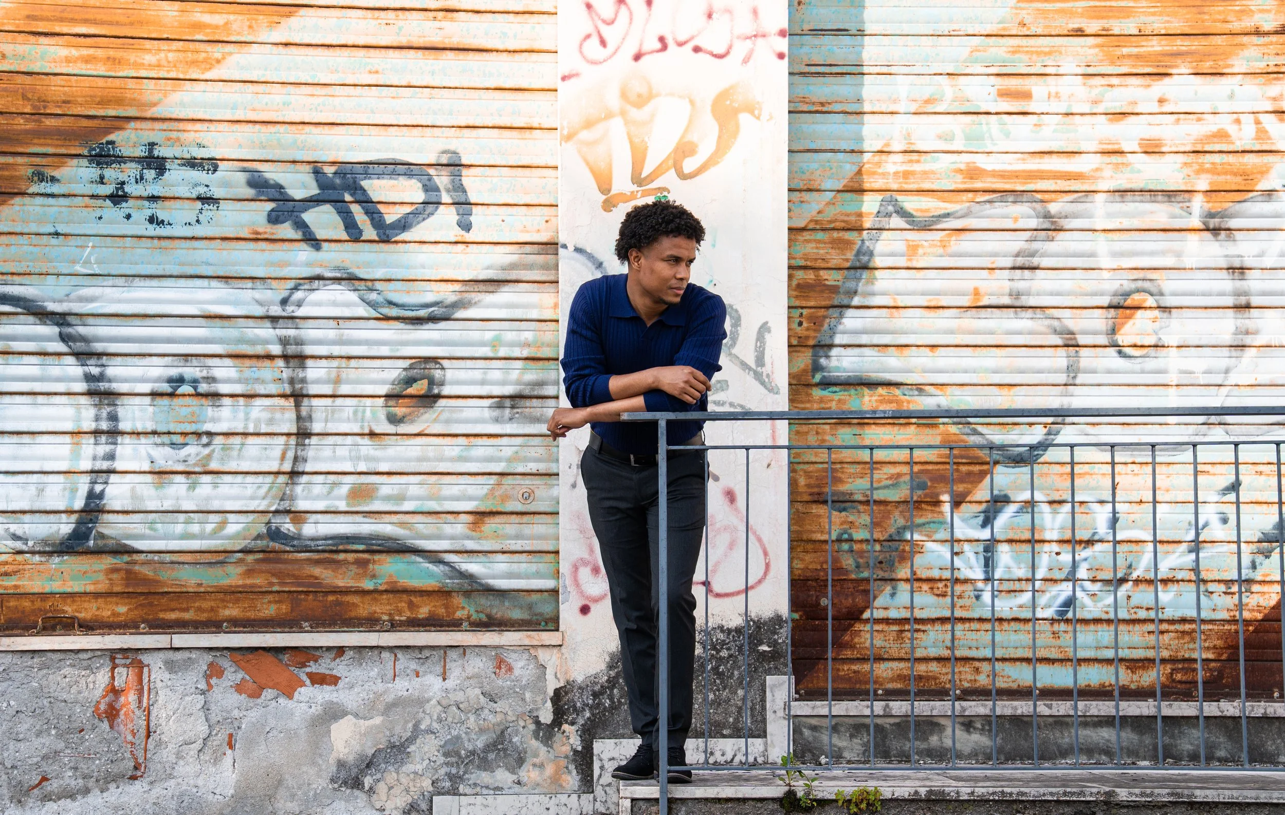 Uomo che si appoggia a una ringhiera davanti a una saracinesca con graffiti.