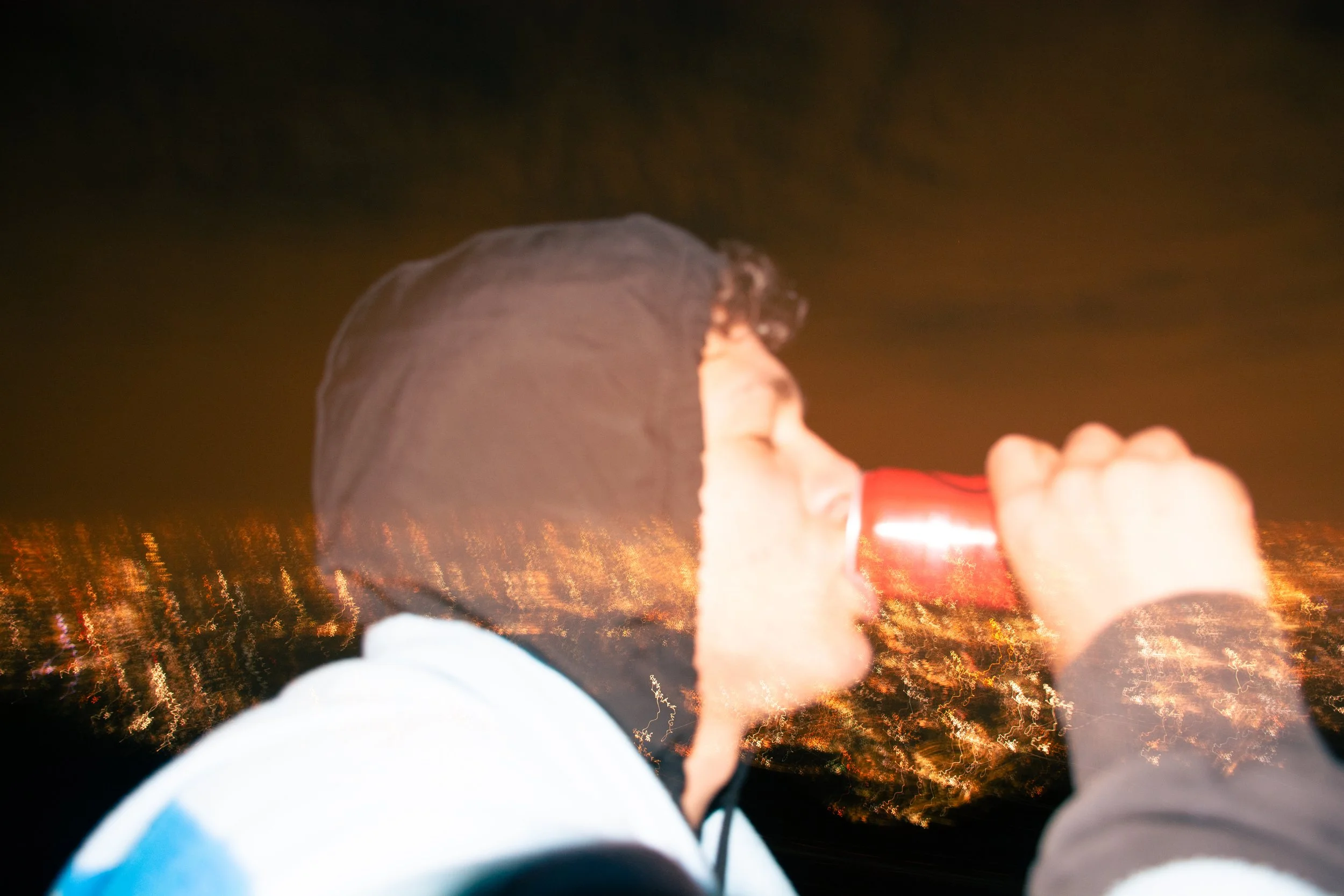 Persona che beve da una lattina rossa in ambientazione notturna, con luci di città sfocate sullo sfondo.