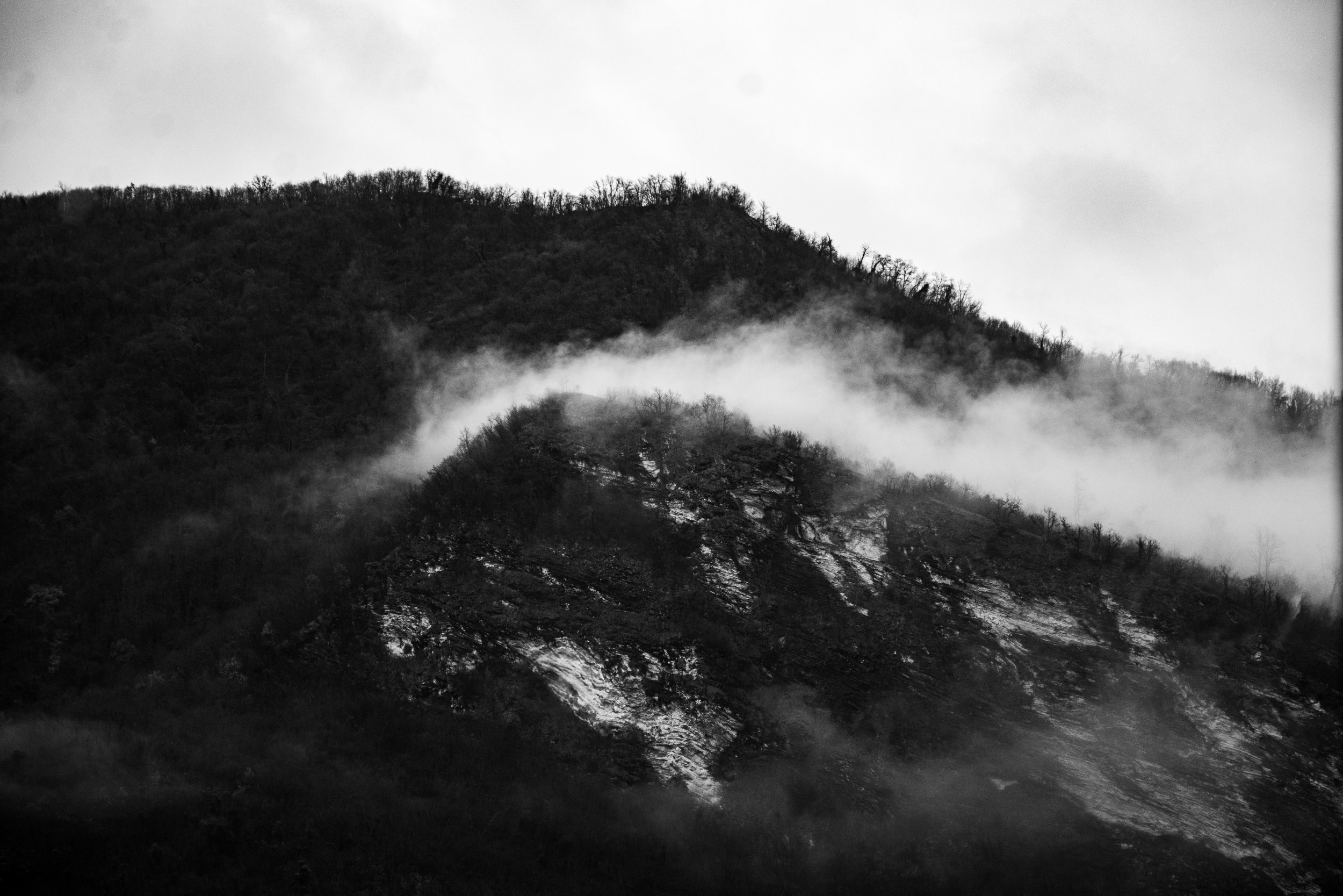 Montagna con alberi spogli e nebbia che si alza tra le pendici