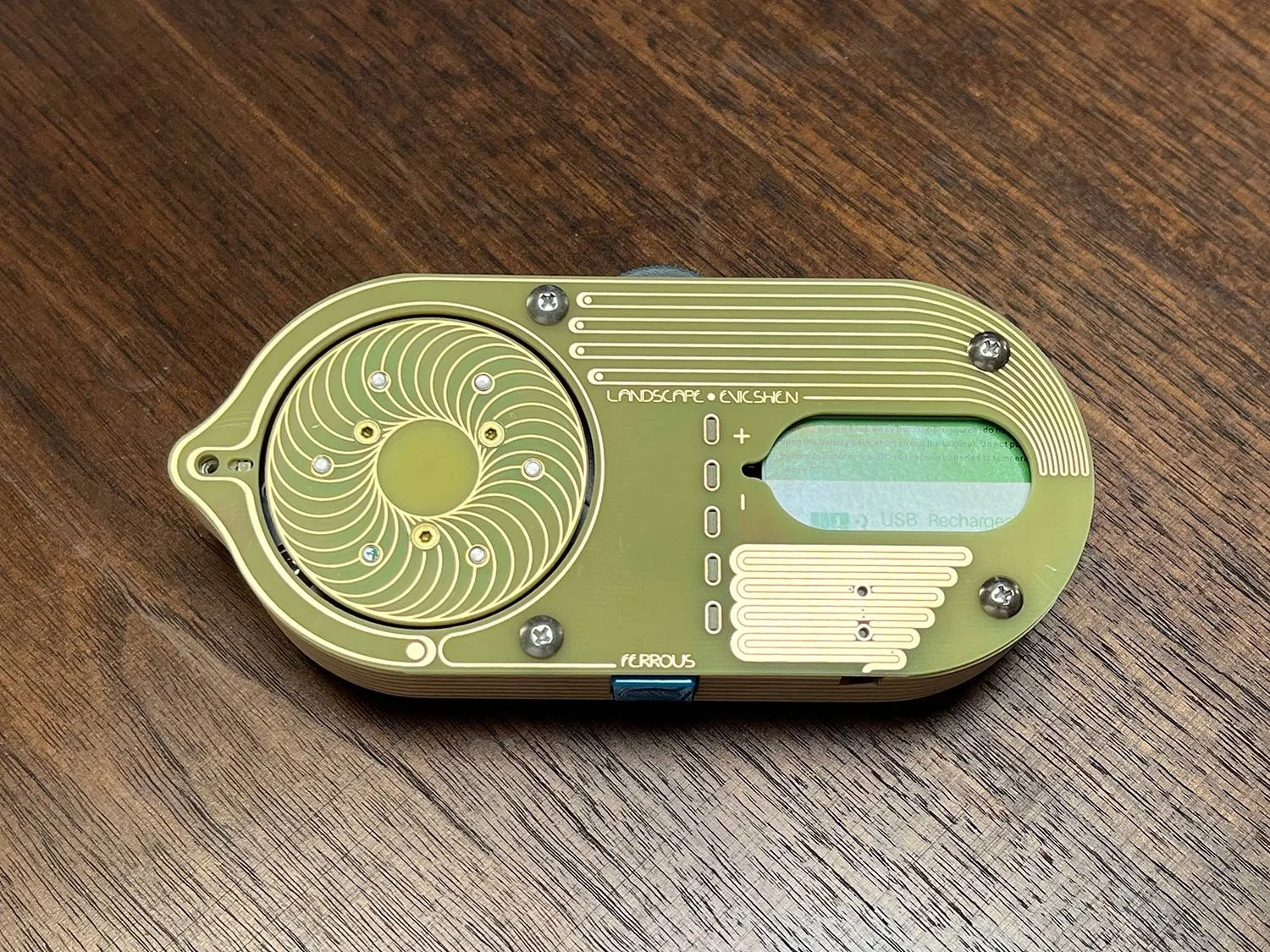 Yellow and gold handheld device (slightly larger than a computer mouse) with a plywood case and spinning magnetic disc. Along each edge is a thumbwheel for speed control and a pulse button. 9 volt battery is exposed through an oval window cutout.