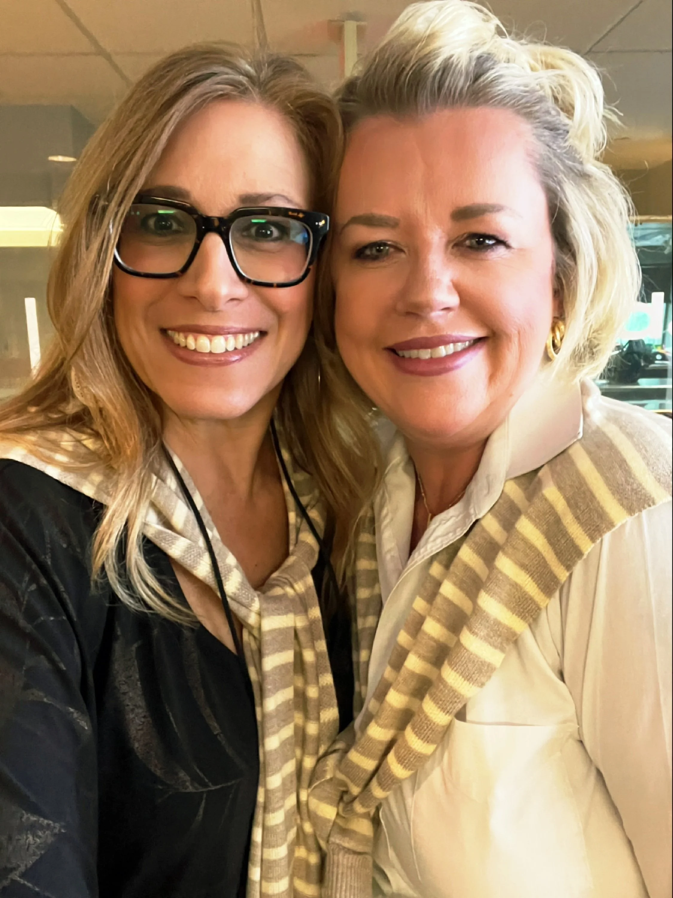 Two women smiling closely for a selfie in a cozy indoor setting.