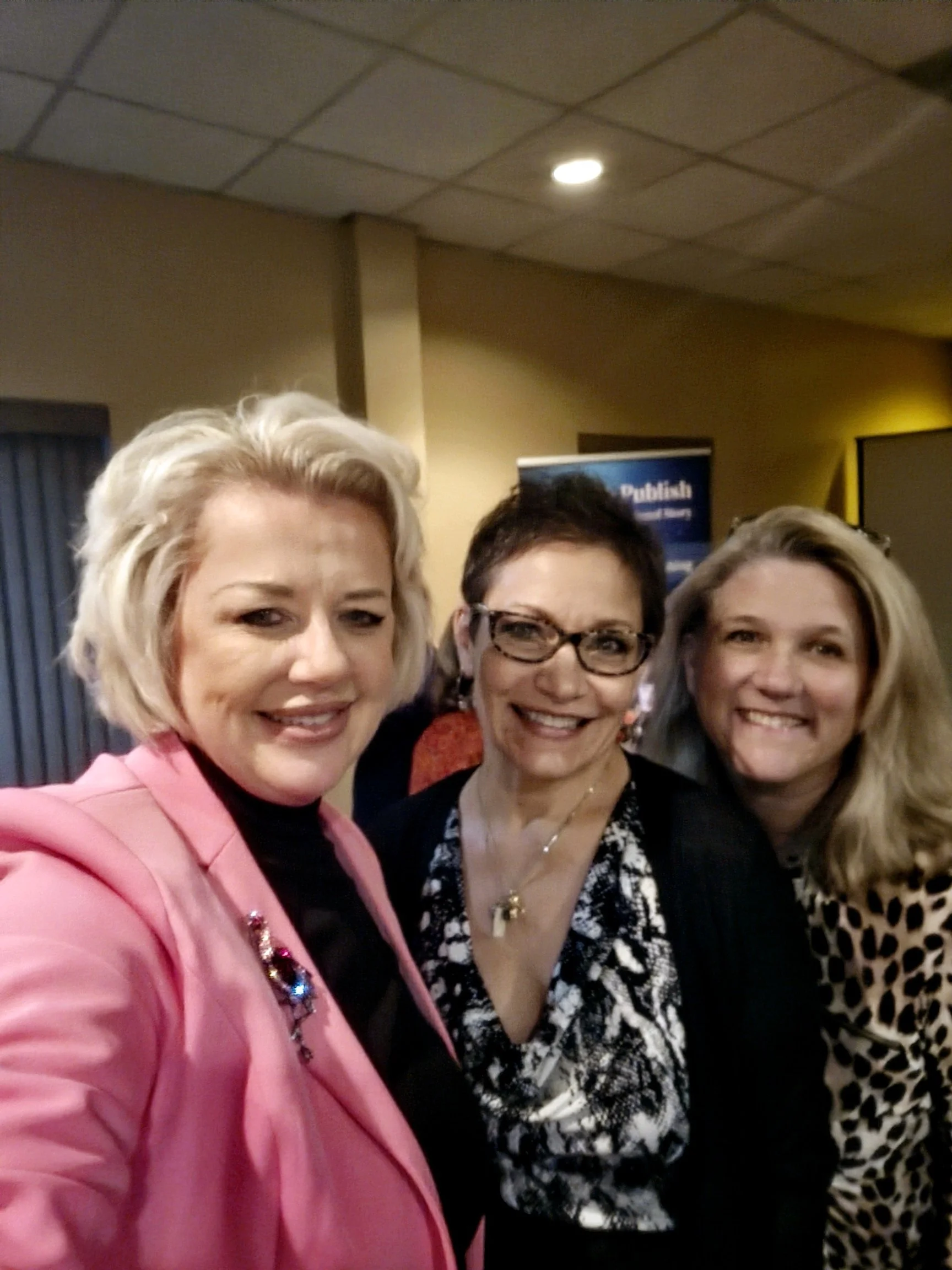 Three women smiling and posing for a selfie at an indoor event.