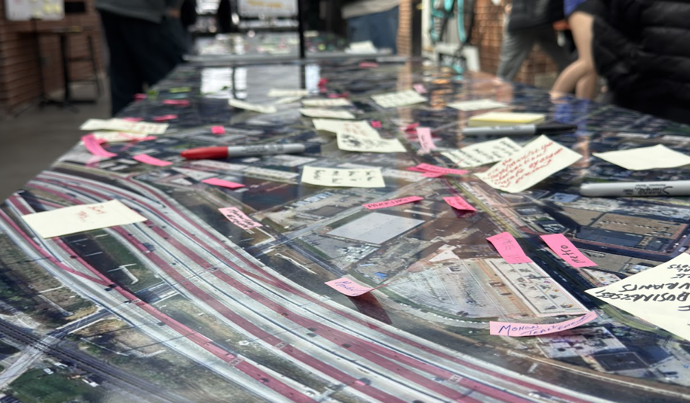 Illustration of a city street with bike lanes, crosswalks, and sidewalks. Details include pedestrians, cyclists, a bus, bicycles, street signs, a church, a dental office, flower pots, and streetlights, with blue outlining for buildings and infrastructure.