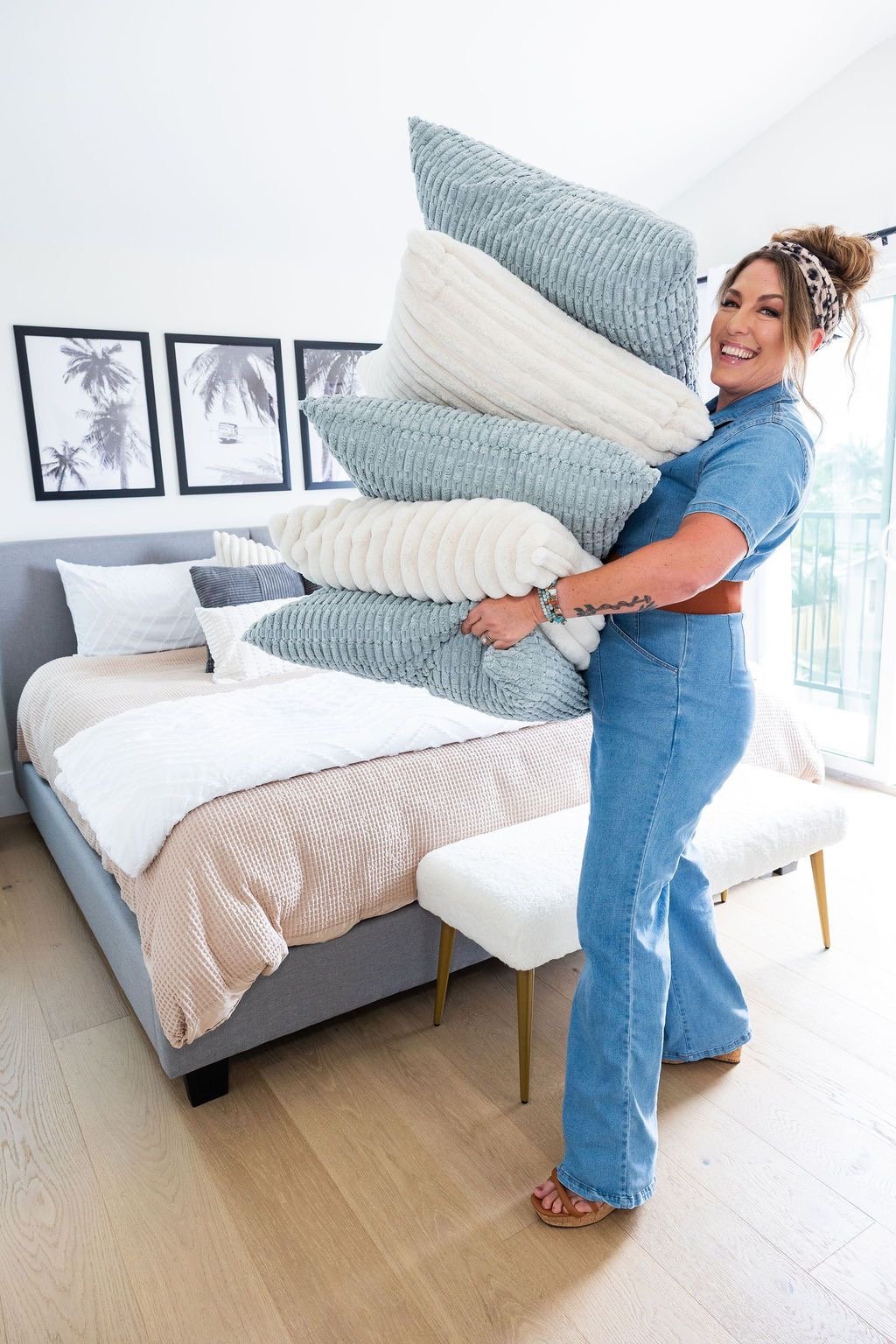 Haus of Heidi owner carrying a stack of blue and white decorative pillows while styling a professionally staged bedroom in North County San Diego.