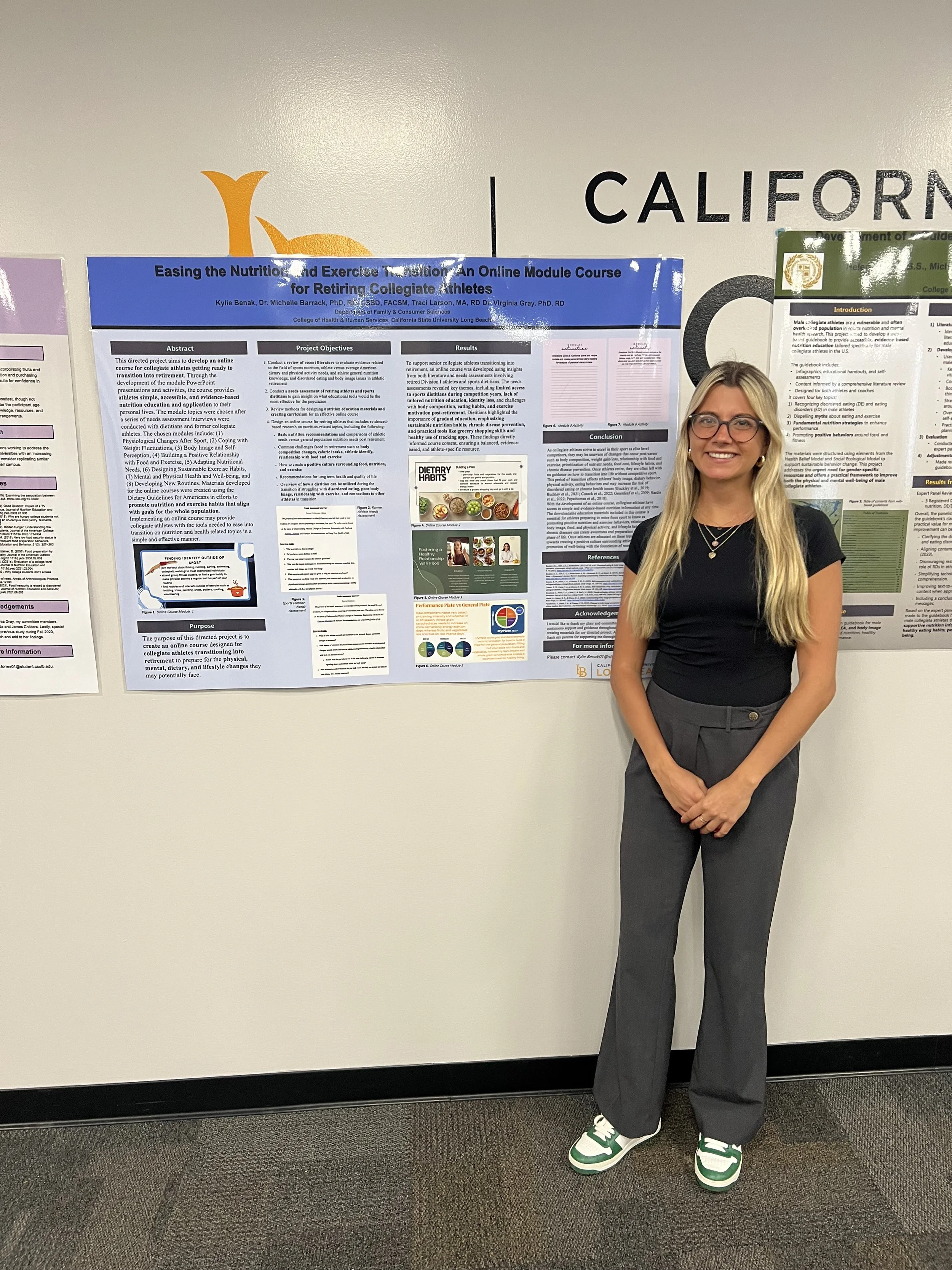 A woman with long blonde hair, glasses, wearing a black t-shirt, gray pants, and green and white sneakers, standing in front of a scientific research poster at an academic or scientific conference.