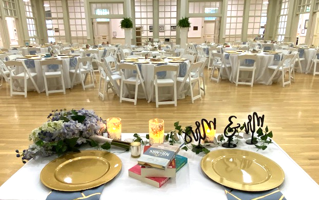 Elegant banquet hall set for a wedding reception with decorated tables, floral arrangements, candles, and personalized name signs.