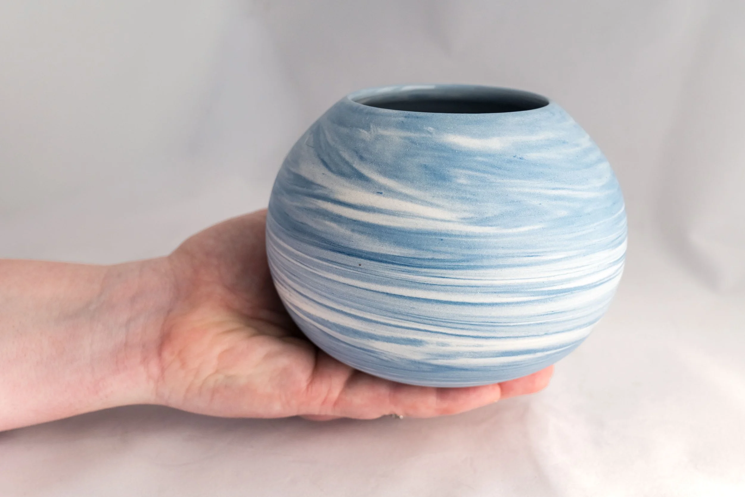 Hand holding a round teal and white porcelain vase on a white background. Copyright Kate O'Rourke