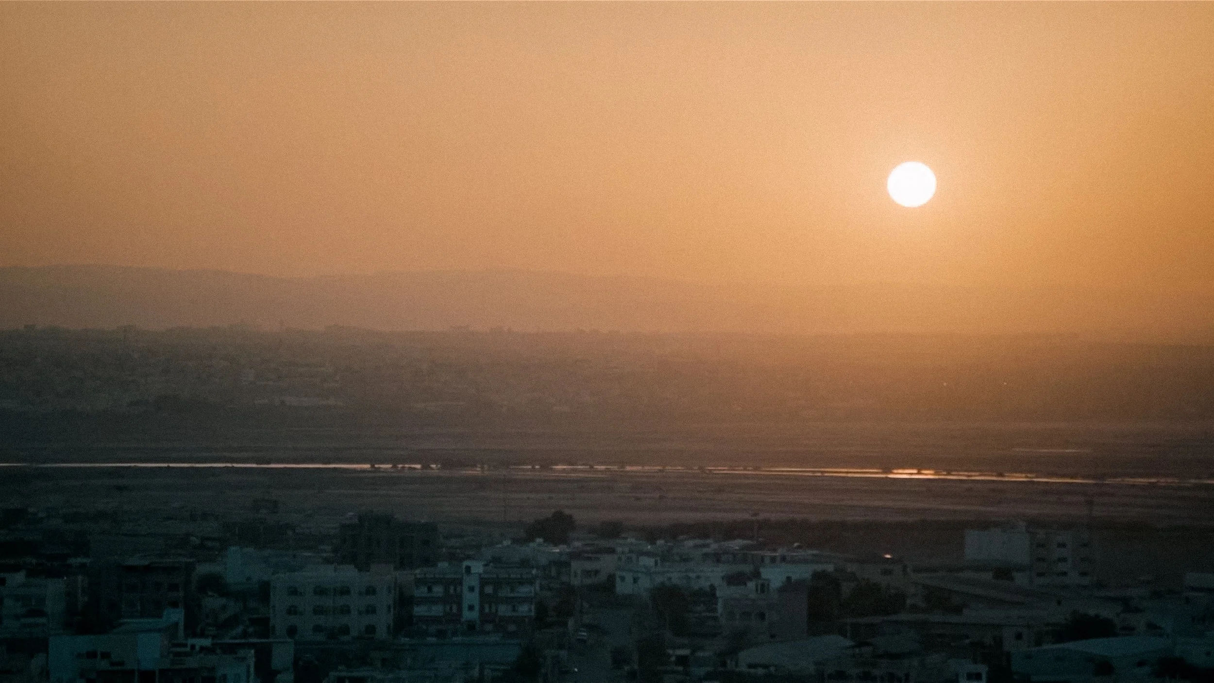 Sunset over a city with buildings in foreground and hills in background