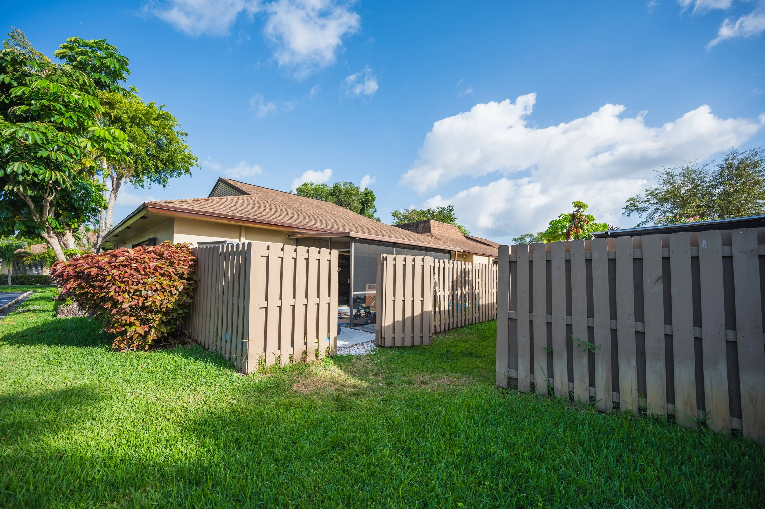 Backyard with a brown backyard fence and a covered patio on a sunny day with a blue sky and white clouds