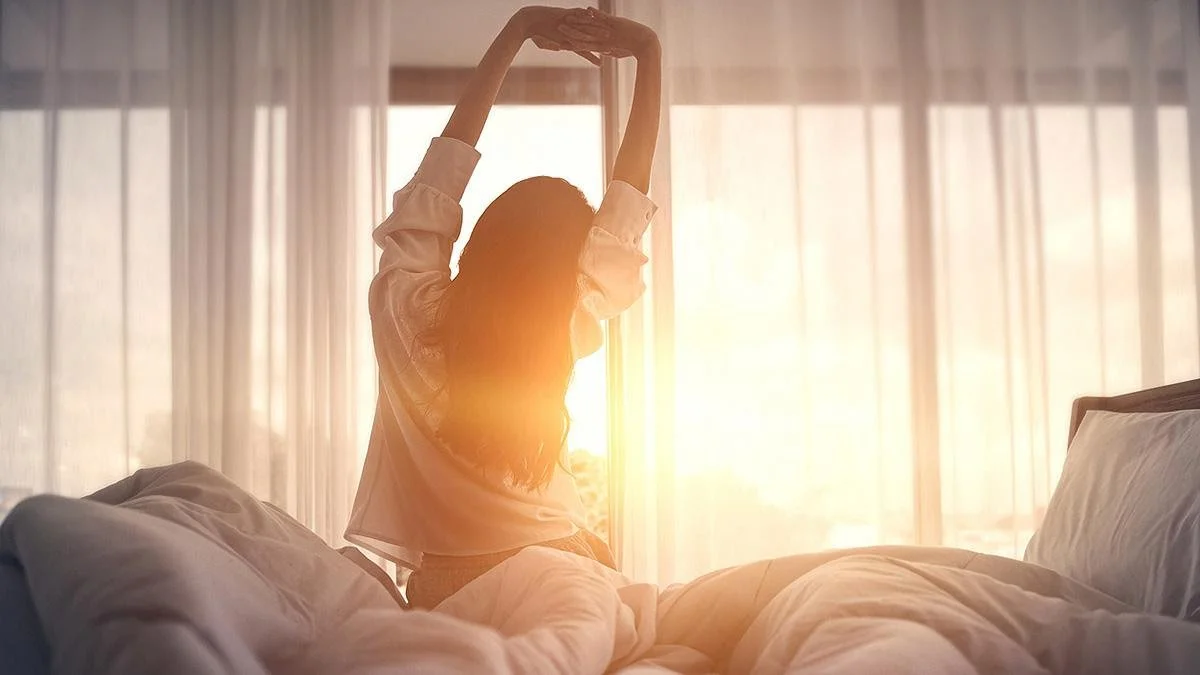 Woman waking up from bed in sunlight