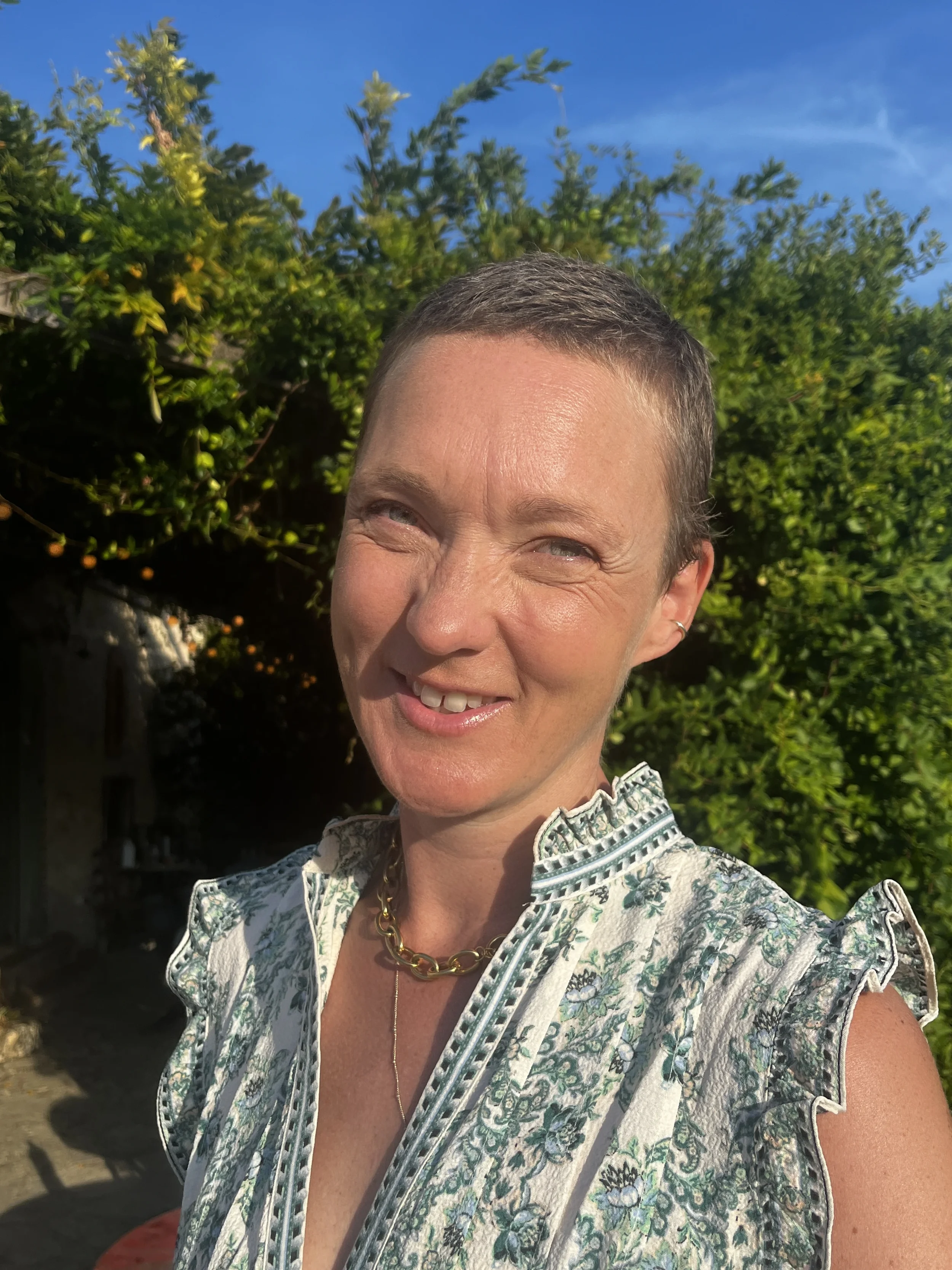  portrait of a woman with cropped hair smiling in the sunshine wearing a floral summer dress.
