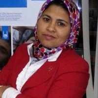 Woman in red blazer and patterned headscarf posing indoors
