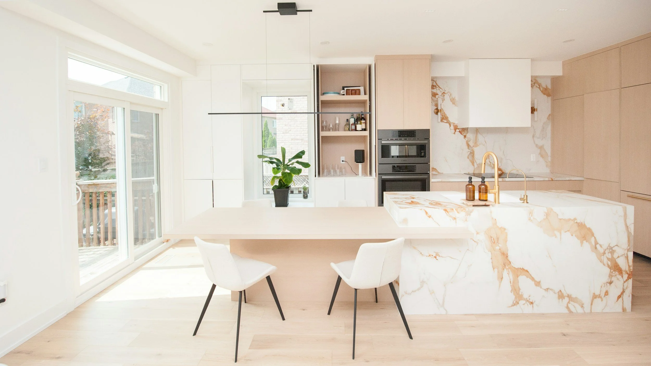 Modern, bright kitchen with a marble island, white cabinets, and a built-in oven, featuring a sliding glass door leading to an outdoor deck.