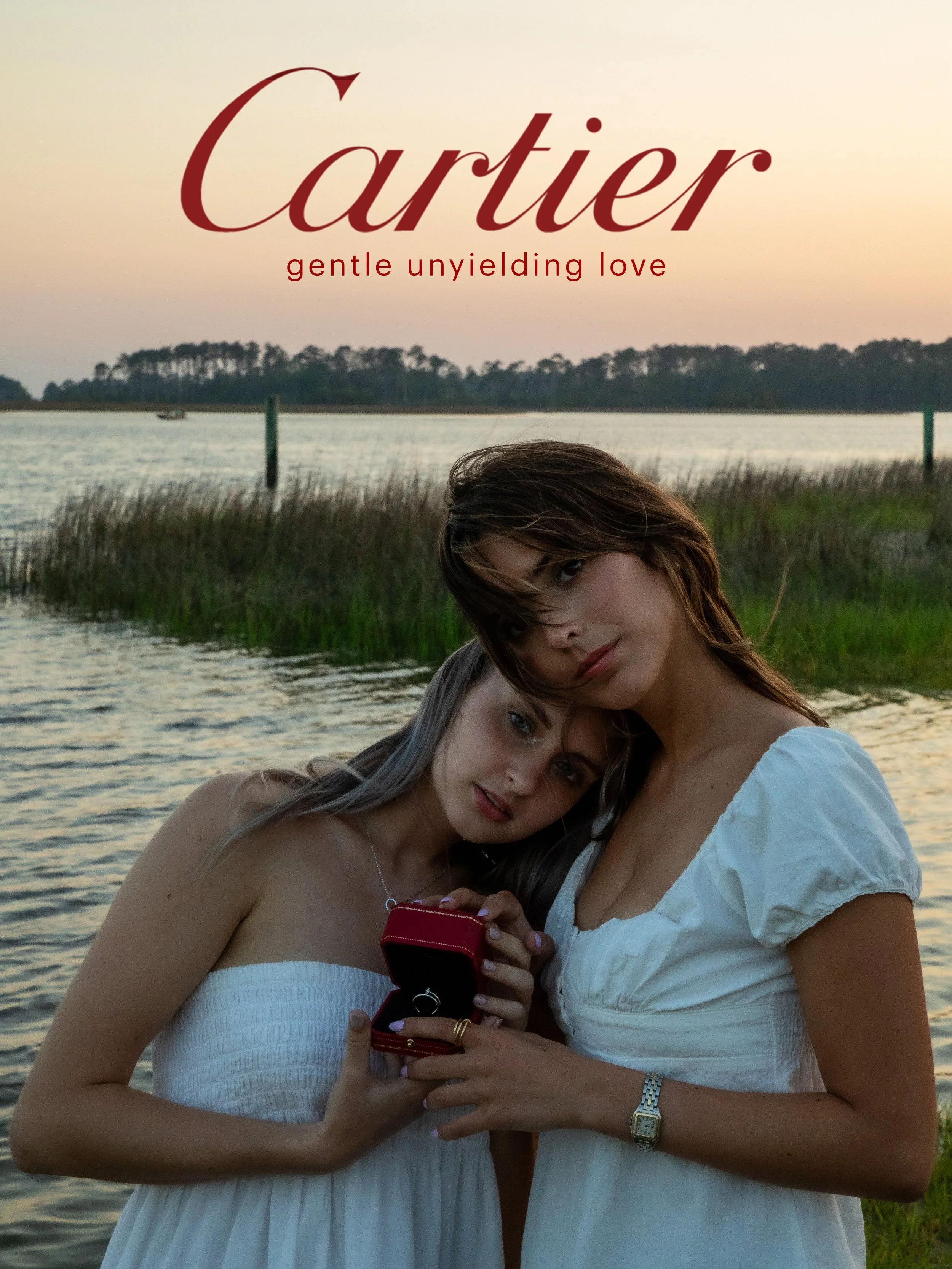 Two women in white dresses standing by a body of water during sunset, holding a small red jewelry box, with the word 'Cartier' and the phrase 'gentle unyielding love' written at the top.