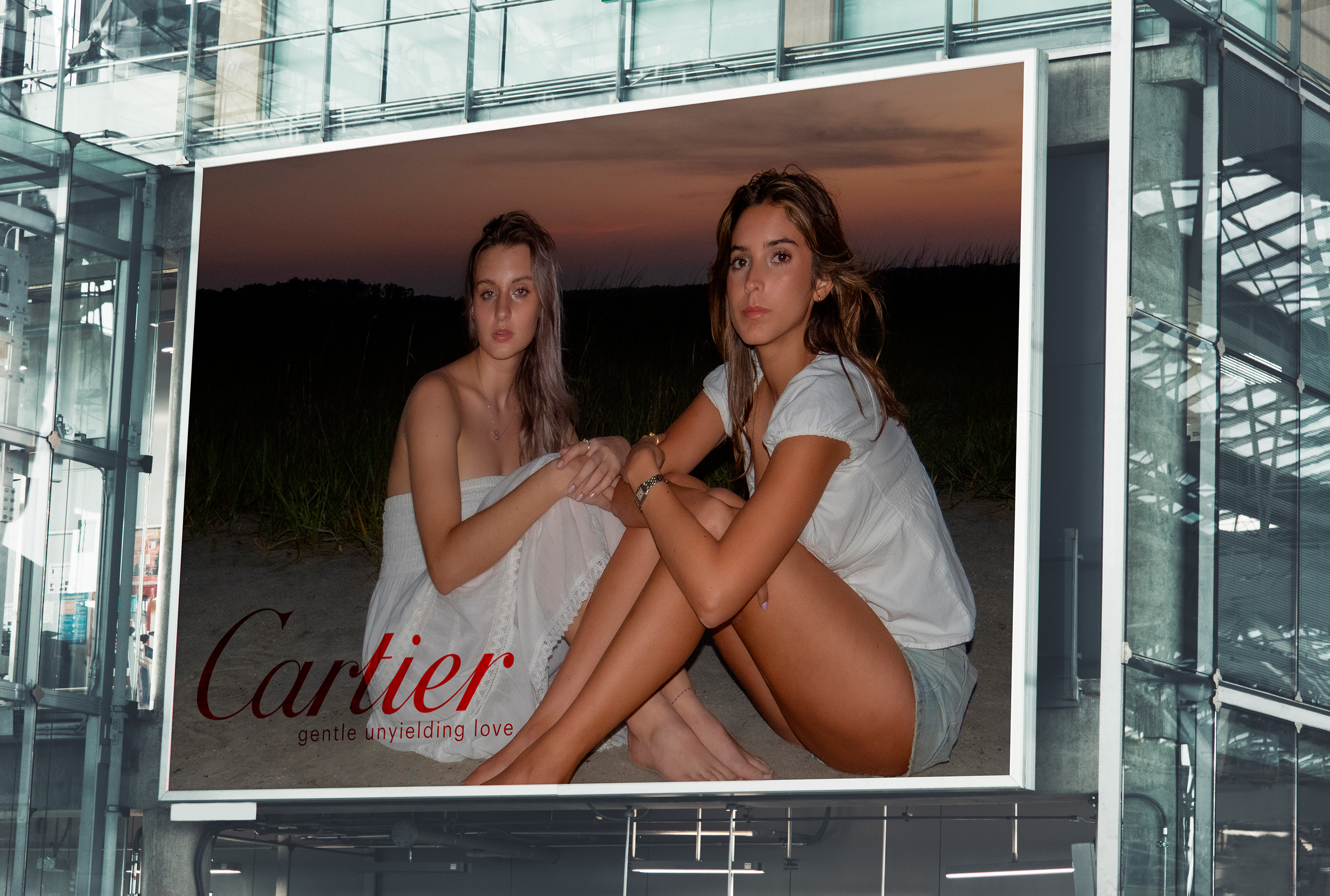 Billboard advertisement for Cartier featuring two young women sitting on the ground at sunset, dressed in casual clothing, with the Cartier logo and the tagline 'gentle unyielding love'