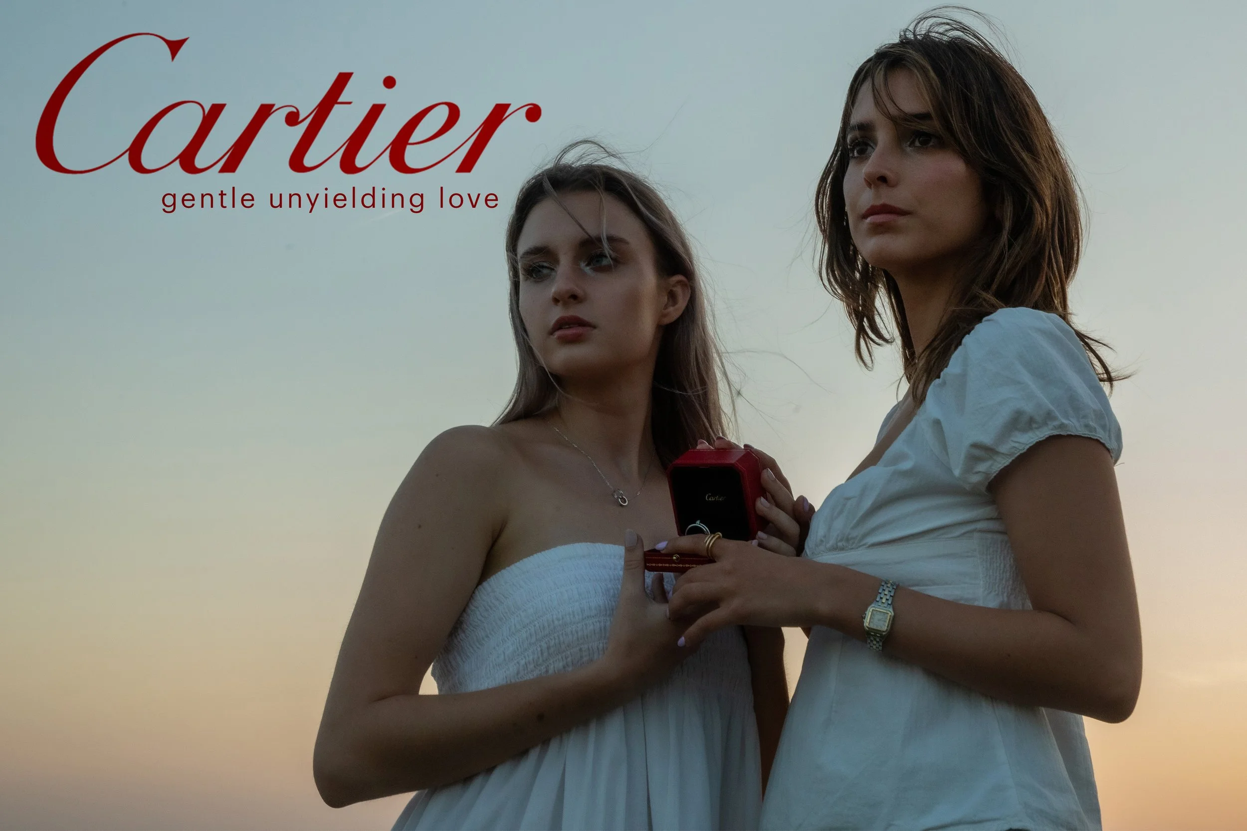 Two women stand outdoors during sunset, one with long brown hair and the other with shoulder-length brown hair, holding a jewelry box with a ring, with the word 'Cartier' and the phrase 'gentle unyielding love' in red text in the top left corner.