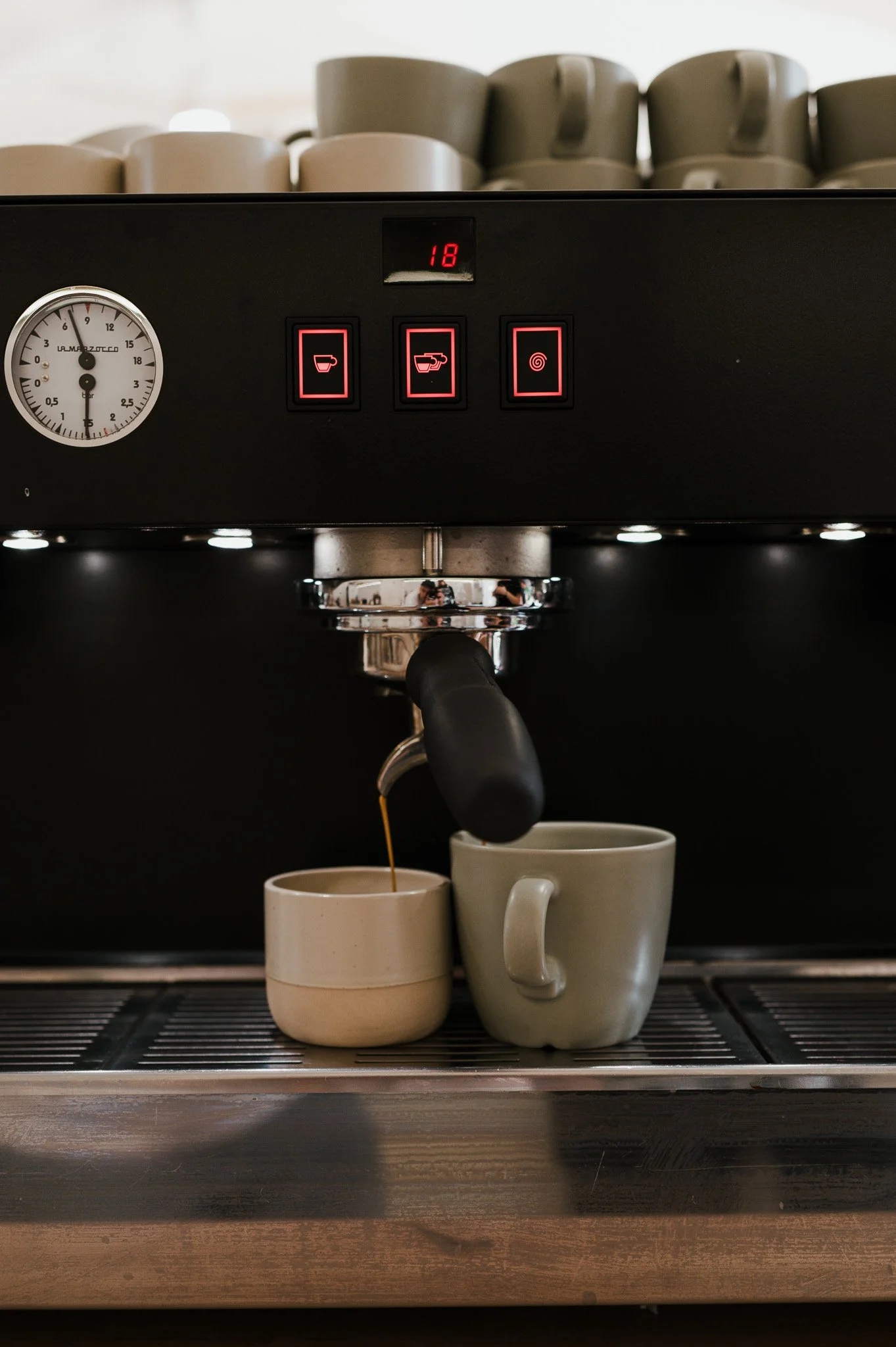 Ein Espressomaschine in Betrieb, die Kaffee in zwei Tassen einschenkt, mit Tassen oben im Hintergrund.