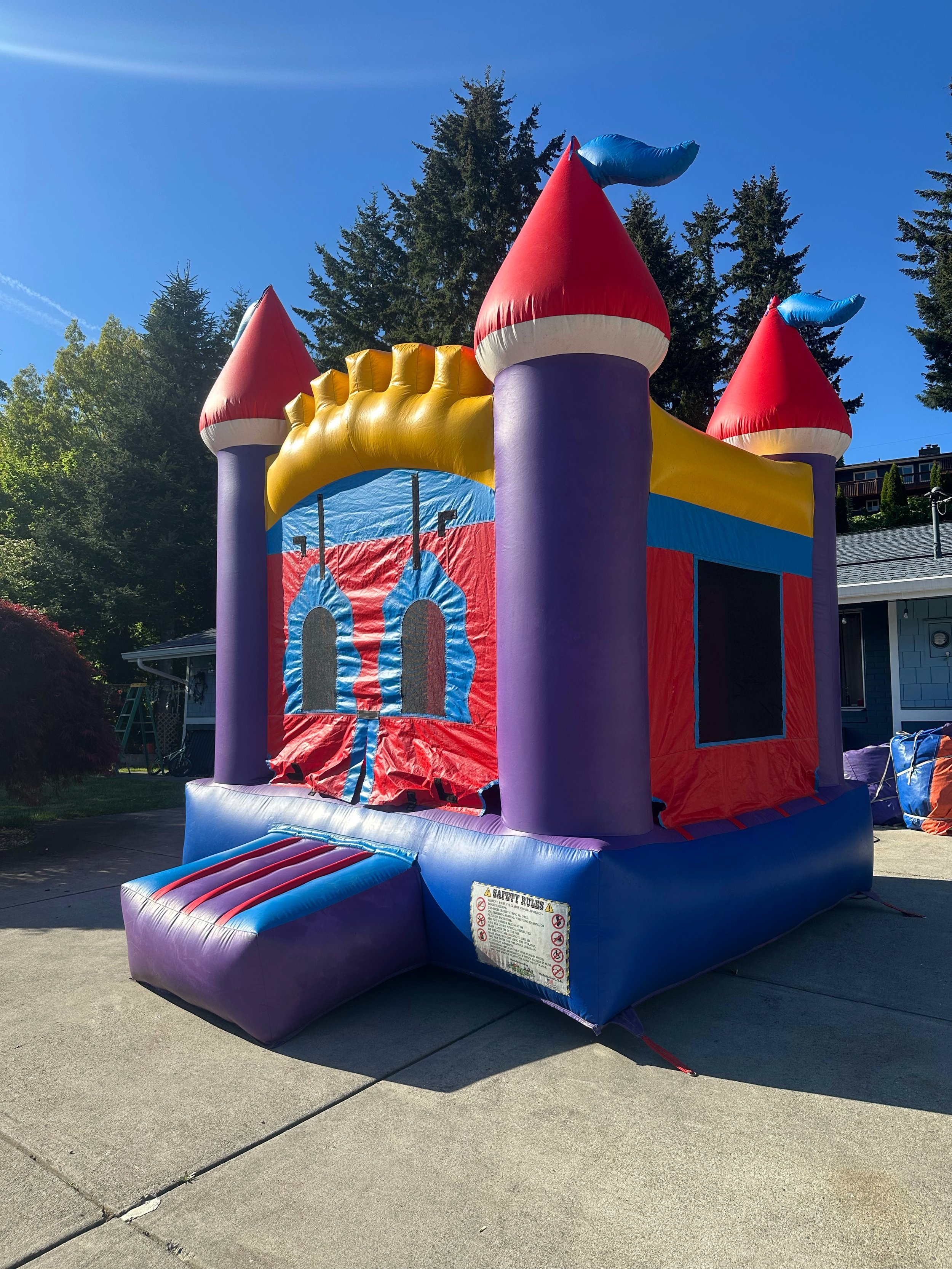 Colorful inflatable bounce house designed as a castle with red, purple, blue, and yellow elements, set up outdoors on a concrete surface.