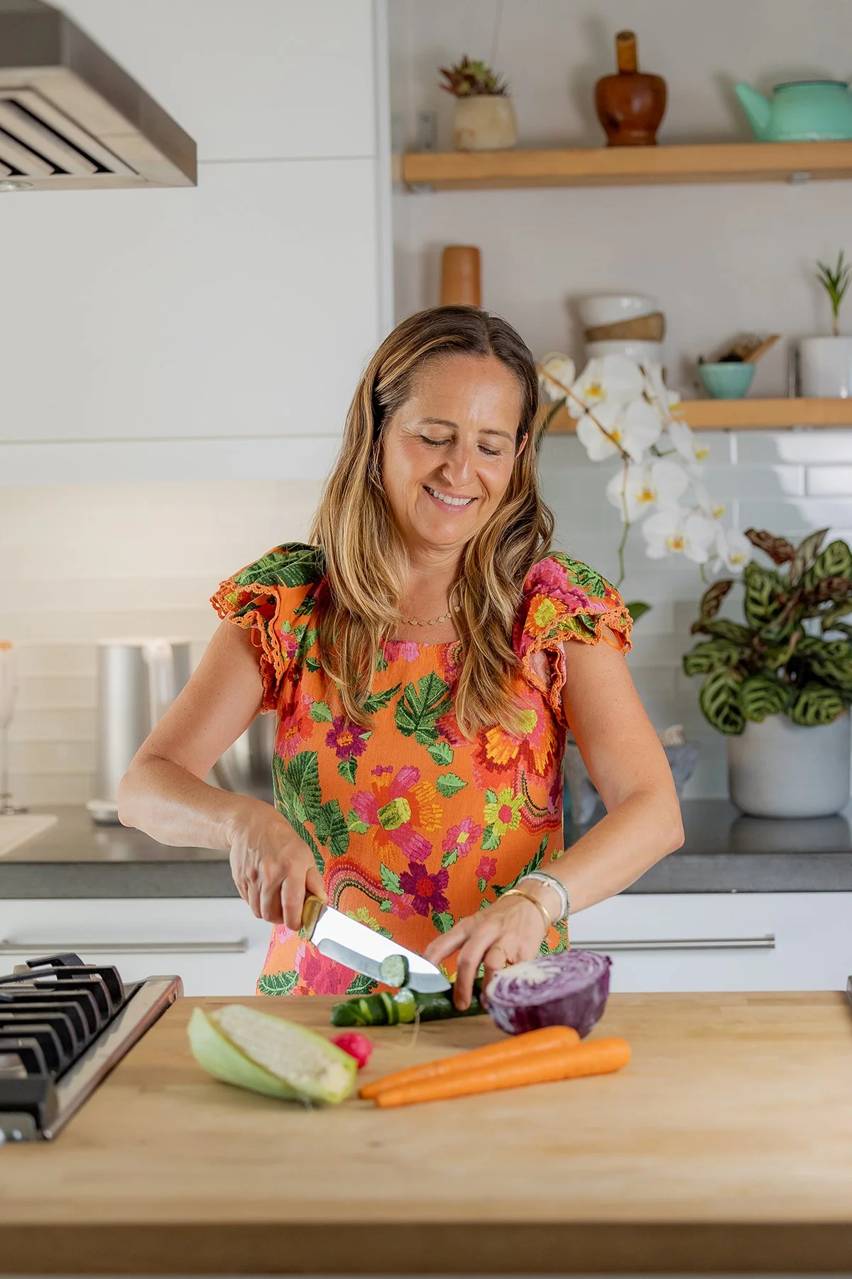 A woman in a colorful floral dress chopping vegetables in a modern kitchen.