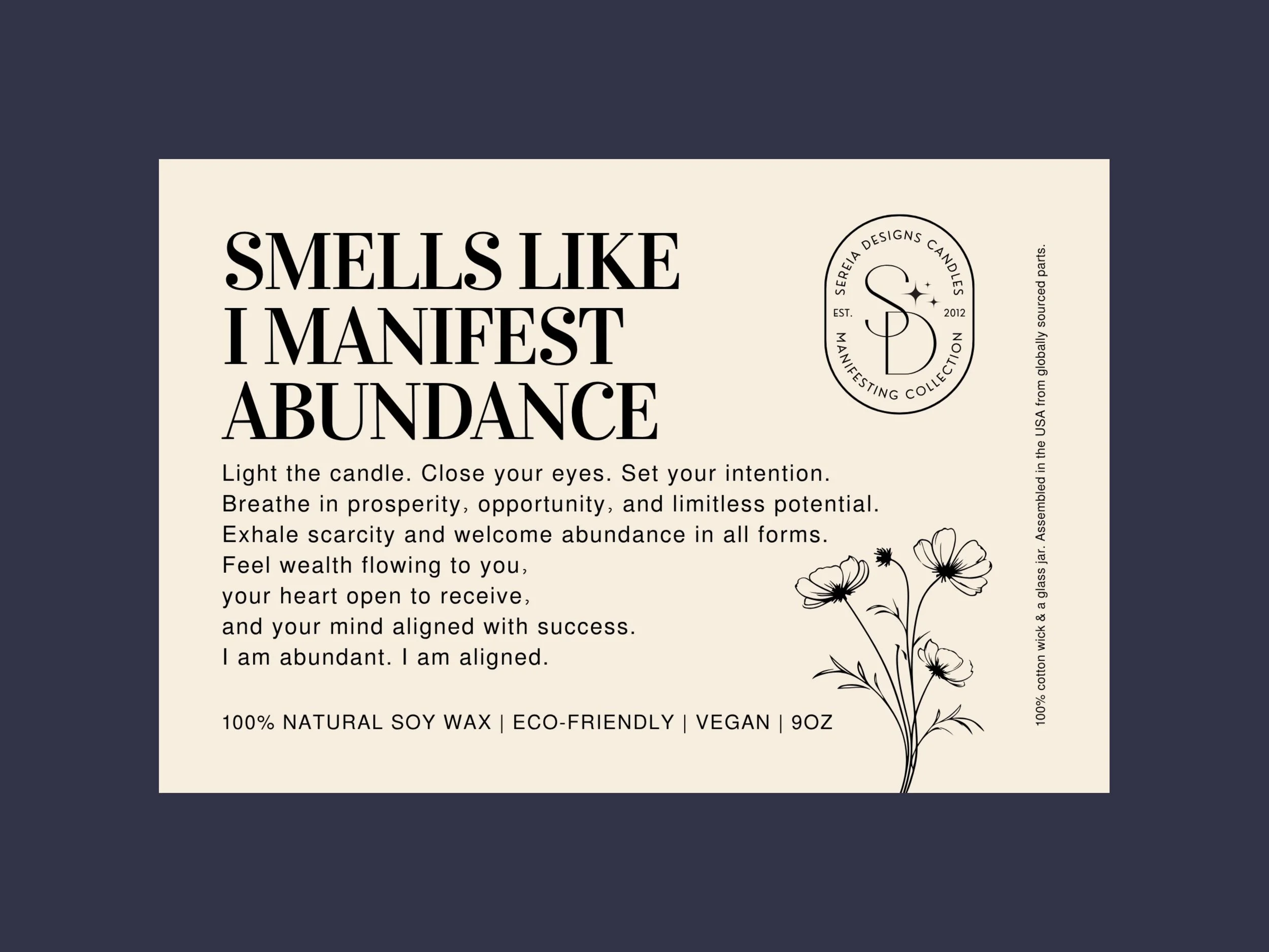 A label for Sereria Designs candles featuring the phrase 'Smells like I manifest abundance' with candle burning instructions, a floral illustration, and information about the candle being natural soy wax, eco-friendly, vegan, and 9 ounces.