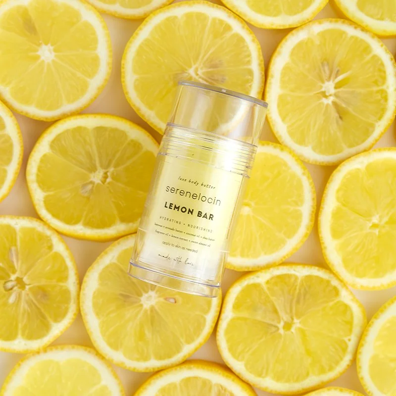 A jar of lemon-scented body butter placed on a surface surrounded by lemon slices.