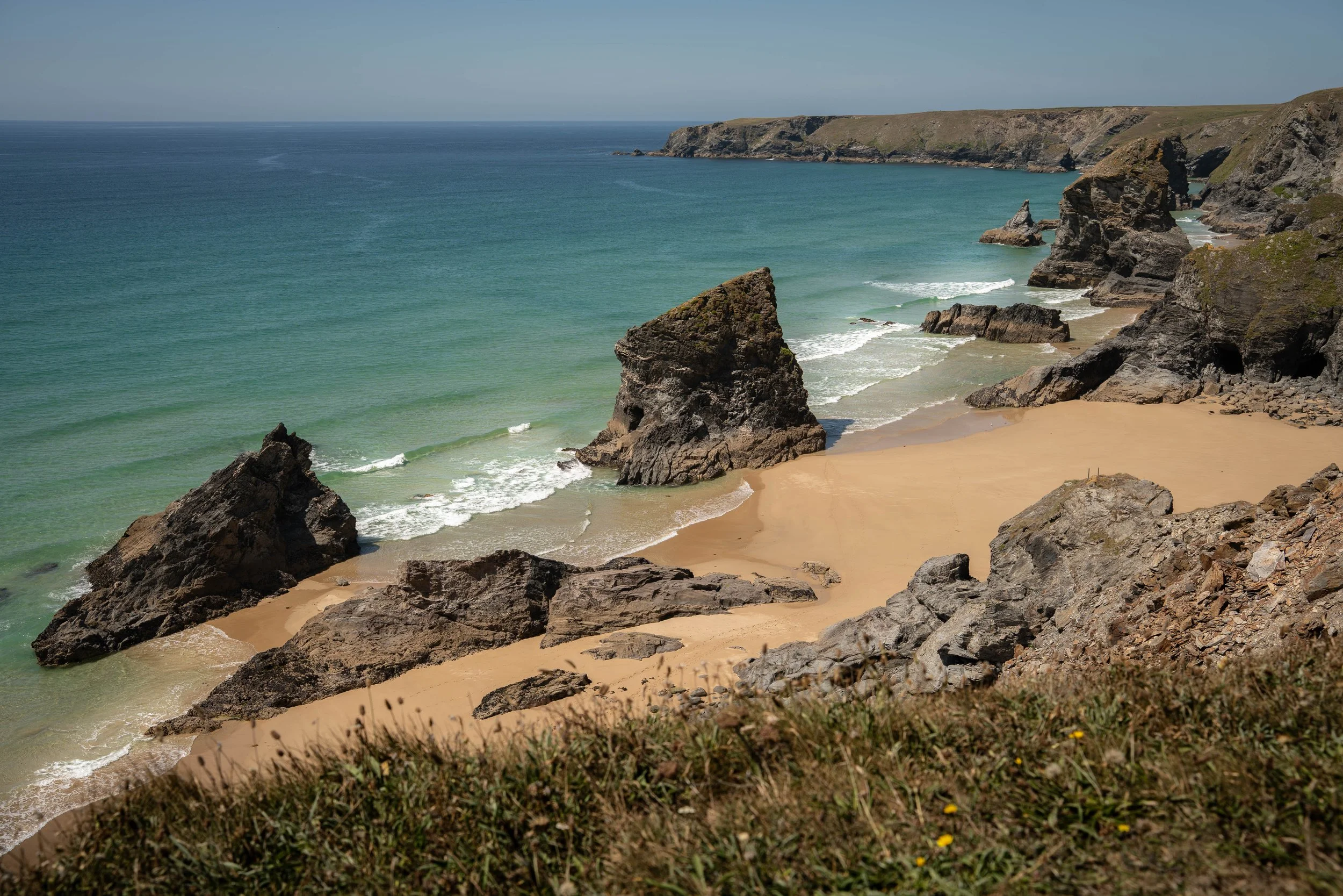 Breathe, Deep Rest and Sound Bath depicted by a view of a sandy beach with large rocks and cliffs, greenish water, and a cloudy sky.