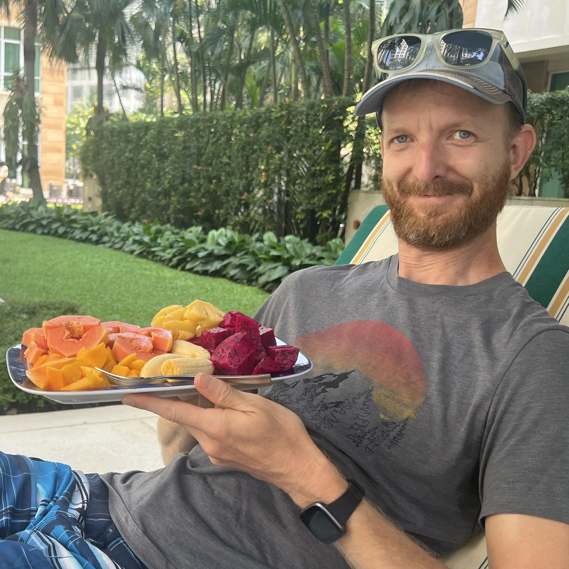 James is smiling and holding a plate of sliced tropical fruit.