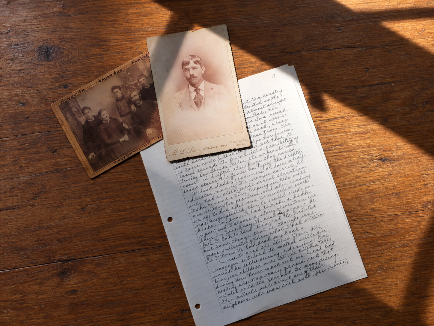 Two old family photographs resting on top of a handwritten family memory on a wooden table.