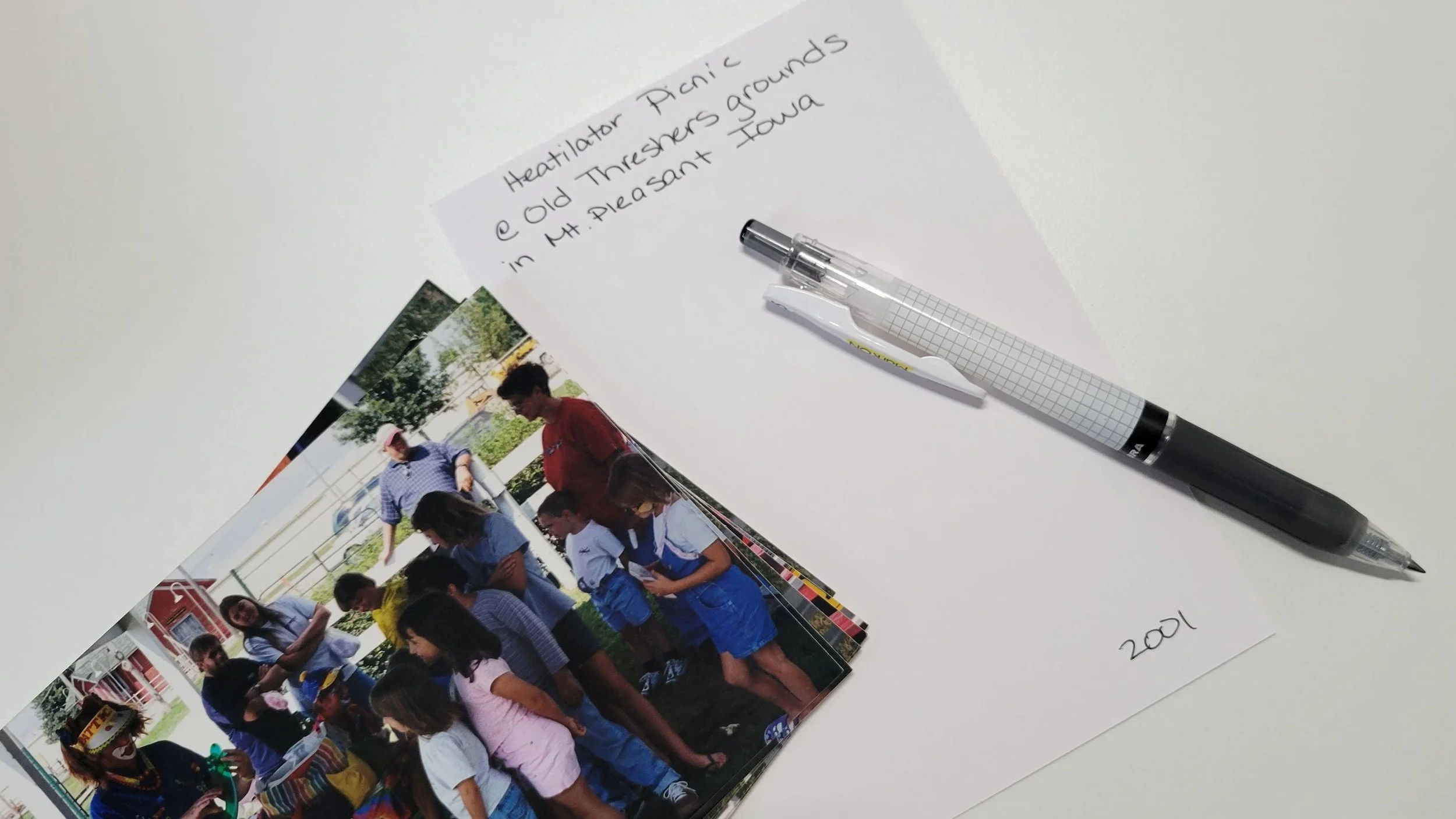 A stack of printed family photos beside a pen and handwritten note cards used to label smaller photo groups.