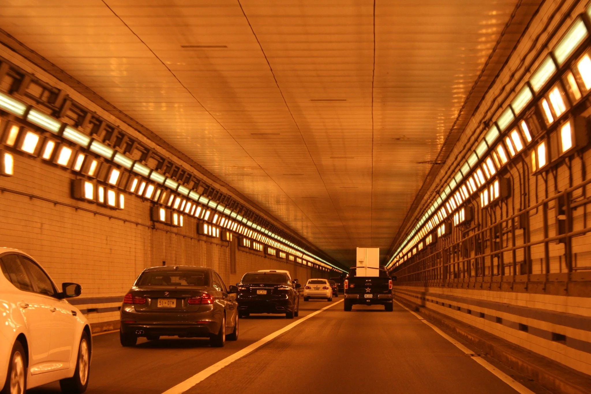 Traffic driving through the Hampton Roads Bridge-Tunnel, lit by warm orange tunnel lights.