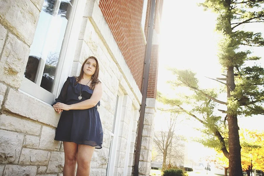 Senior girl leaning against stone wall in soft natural light during senior photo session