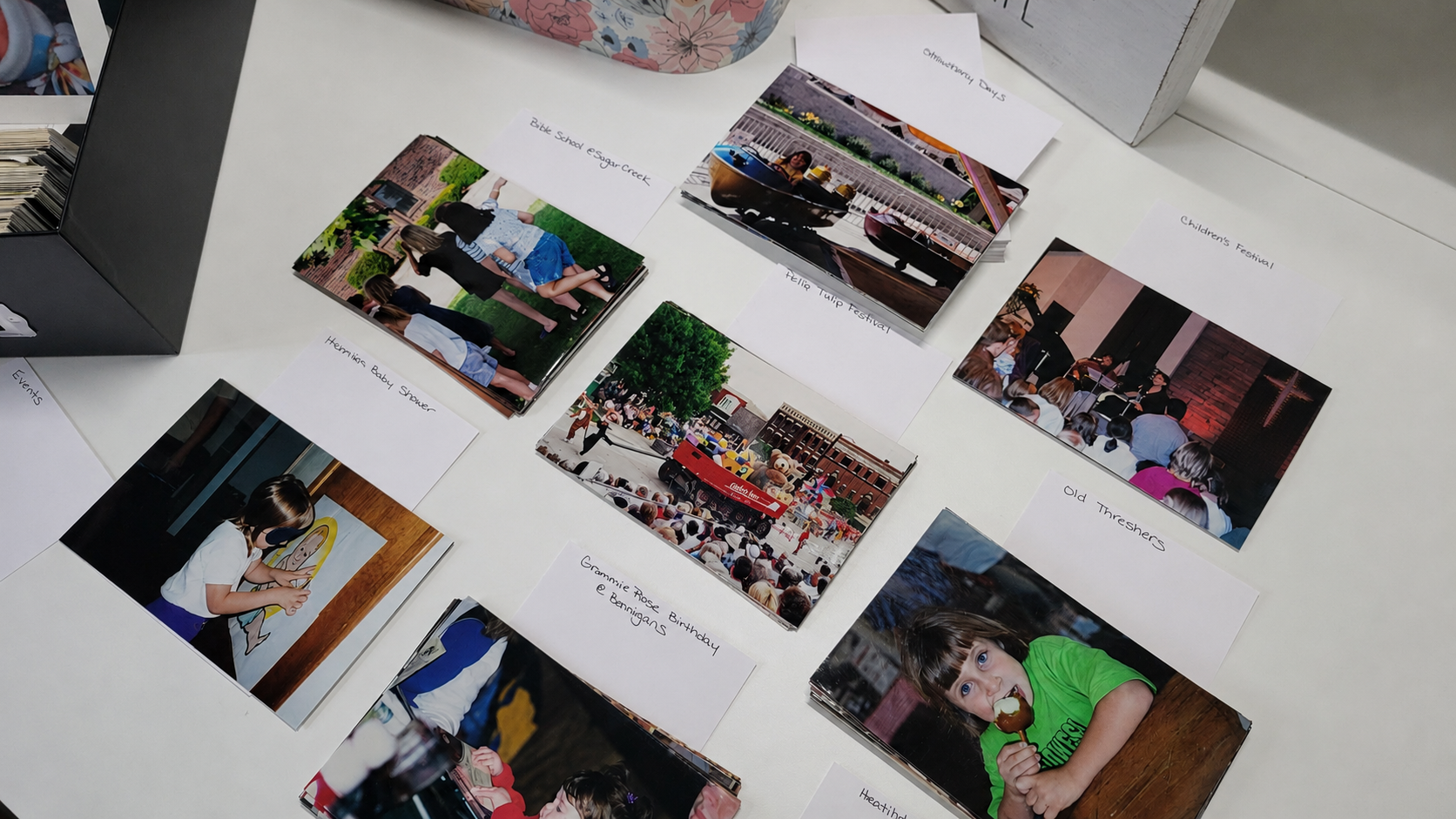Printed family photos spread across a table and sorted into more specific labeled groups with handwritten note cards.