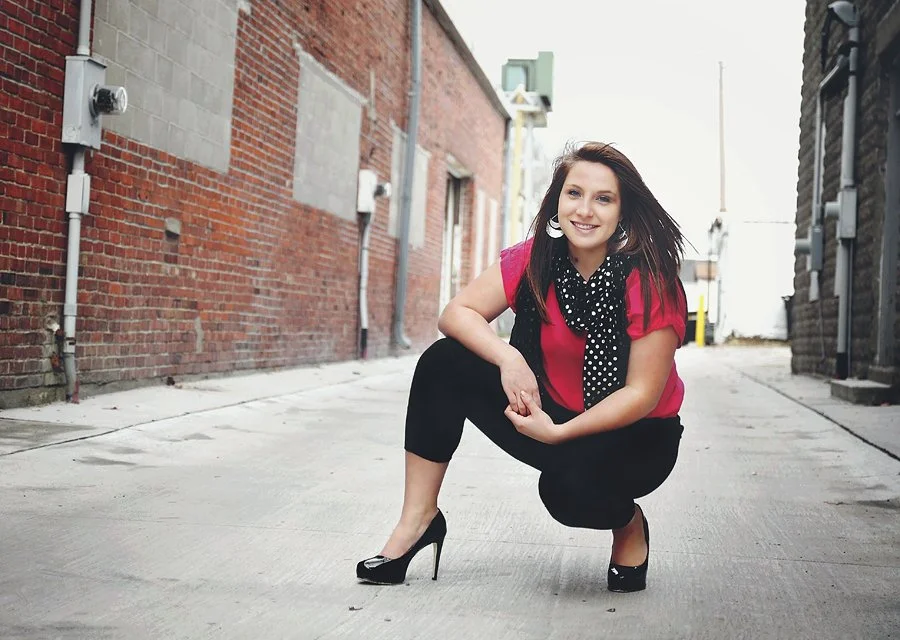 High school senior girl in a red top posing in an urban alley during a senior photo session