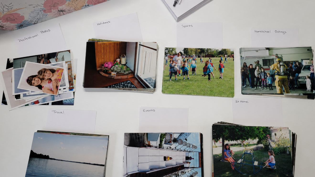 Printed family photos sorted into small labeled categories on a white table, including travel, events, holidays, sports, and at-home photos.