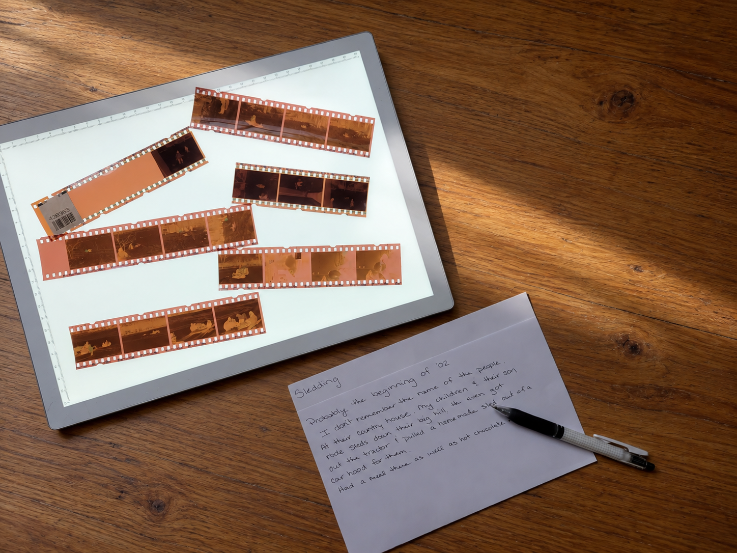 Old film negatives on a light pad next to a handwritten note identifying the event and details.