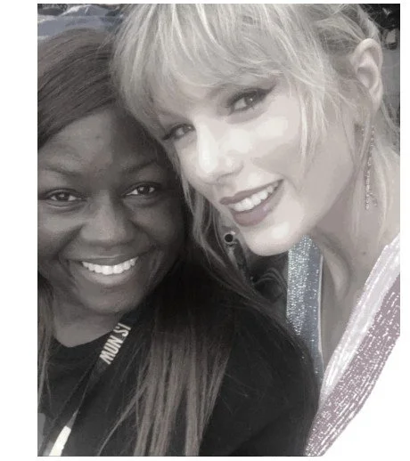 Two women smiling closely for a selfie. One has dark skin and long dark hair; the other has light skin and blonde hair. Both are smiling and looking at the camera.