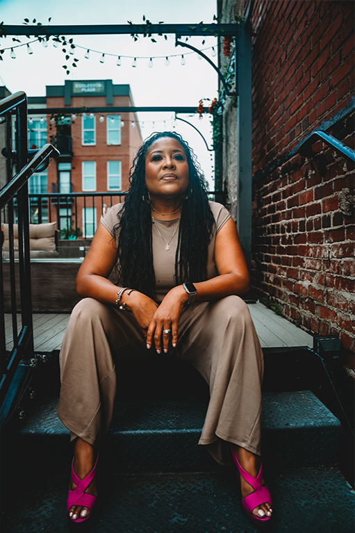 Woman sitting on outdoor staircase on a city rooftop patio with brick walls and buildings in the background.