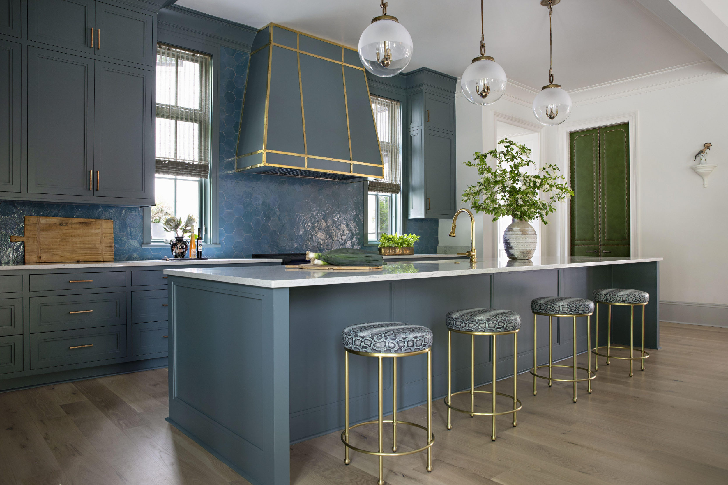 Modern kitchen with blue cabinetry, gold accents, a marble island with bar stools, and a large potted plant on the countertop.