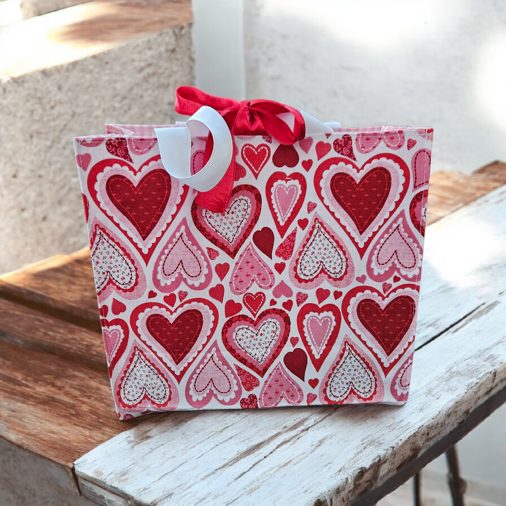 Gift bag decorated with red, pink, and white hearts, tied with red and white ribbons.