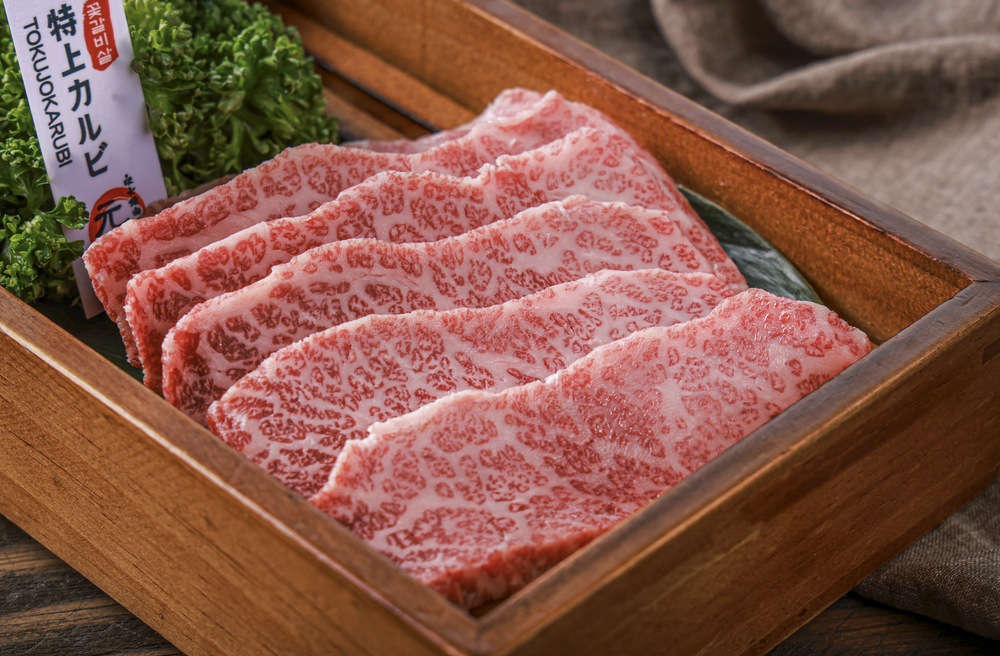Slices of marbled high-quality beef in a wooden box garnished with greens.